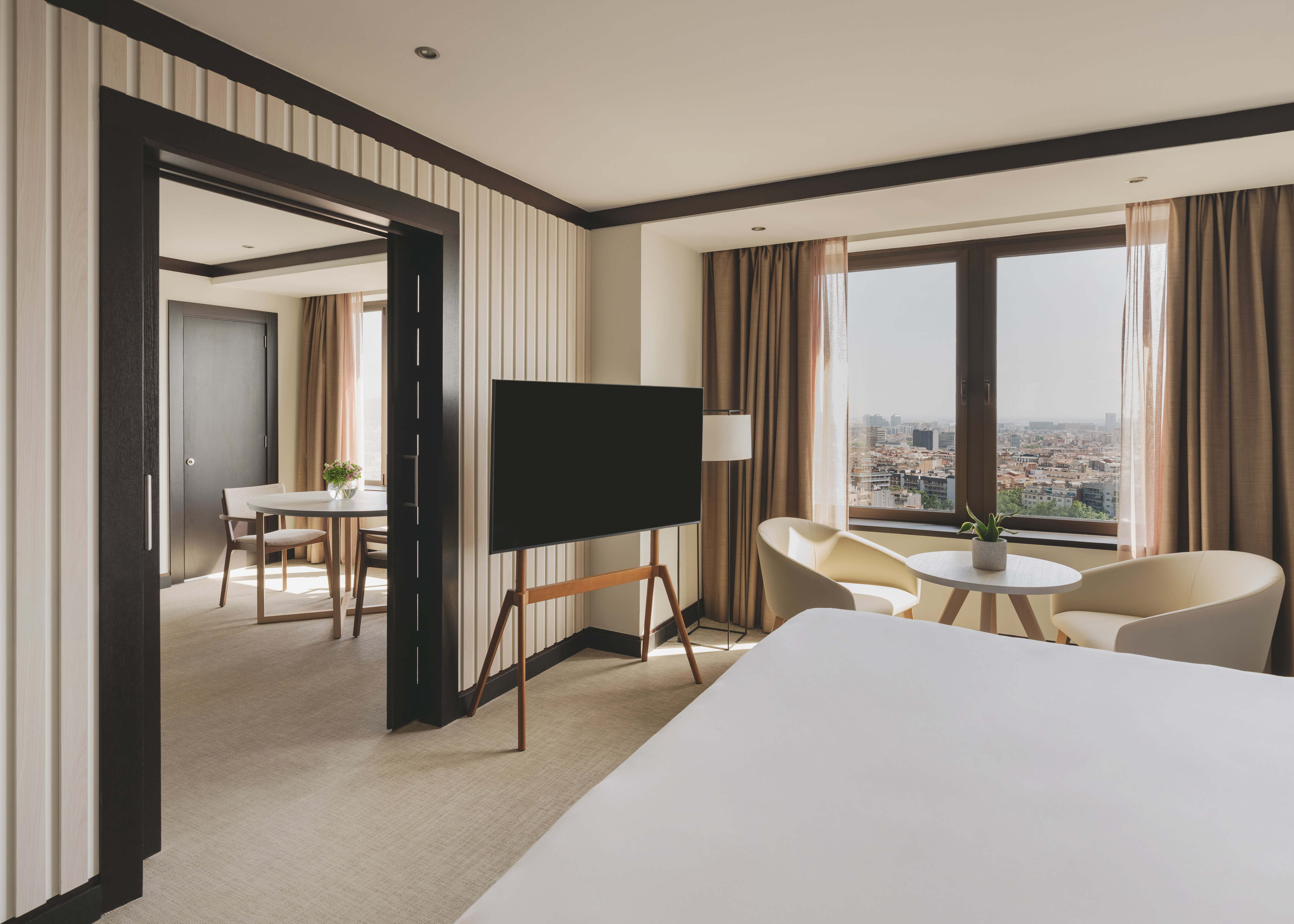 Suite de hotel moderna con dormitorio, TV y vista a la ciudad.