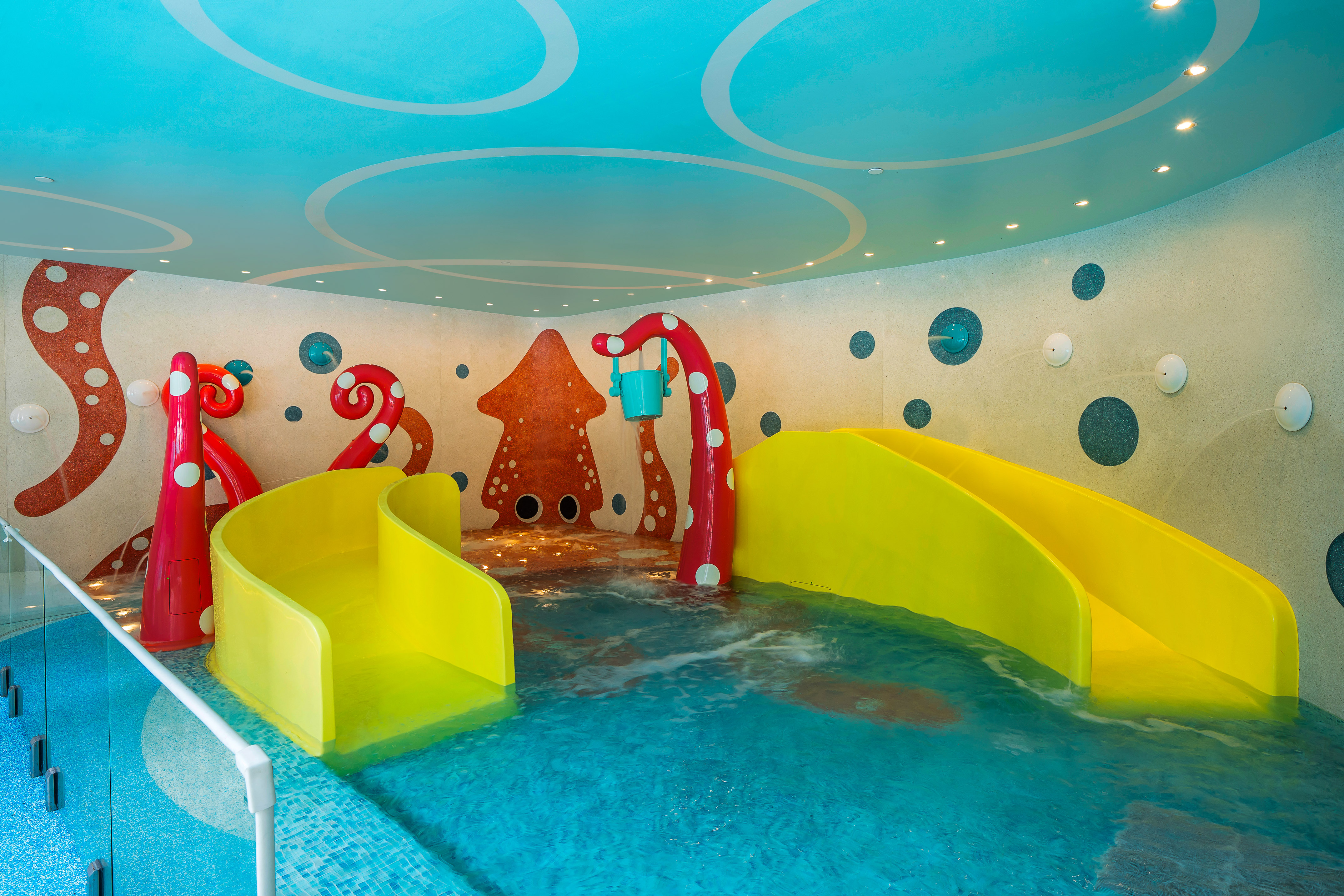 Indoor kids pool with yellow slides, red octopus decor, and blue water play area.
