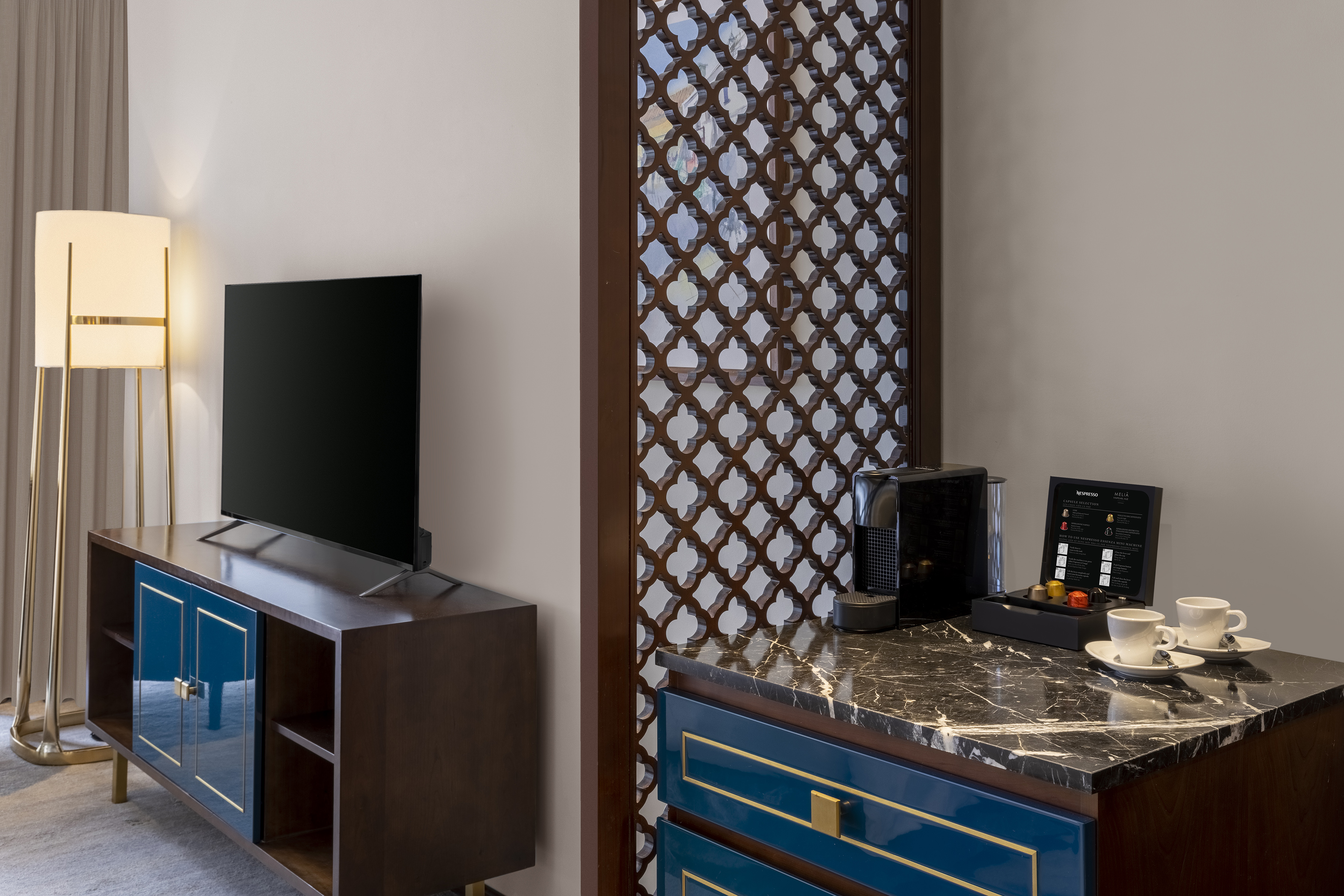 Hotel room with TV, Nespresso machine, elegant blue console, and patterned divider.