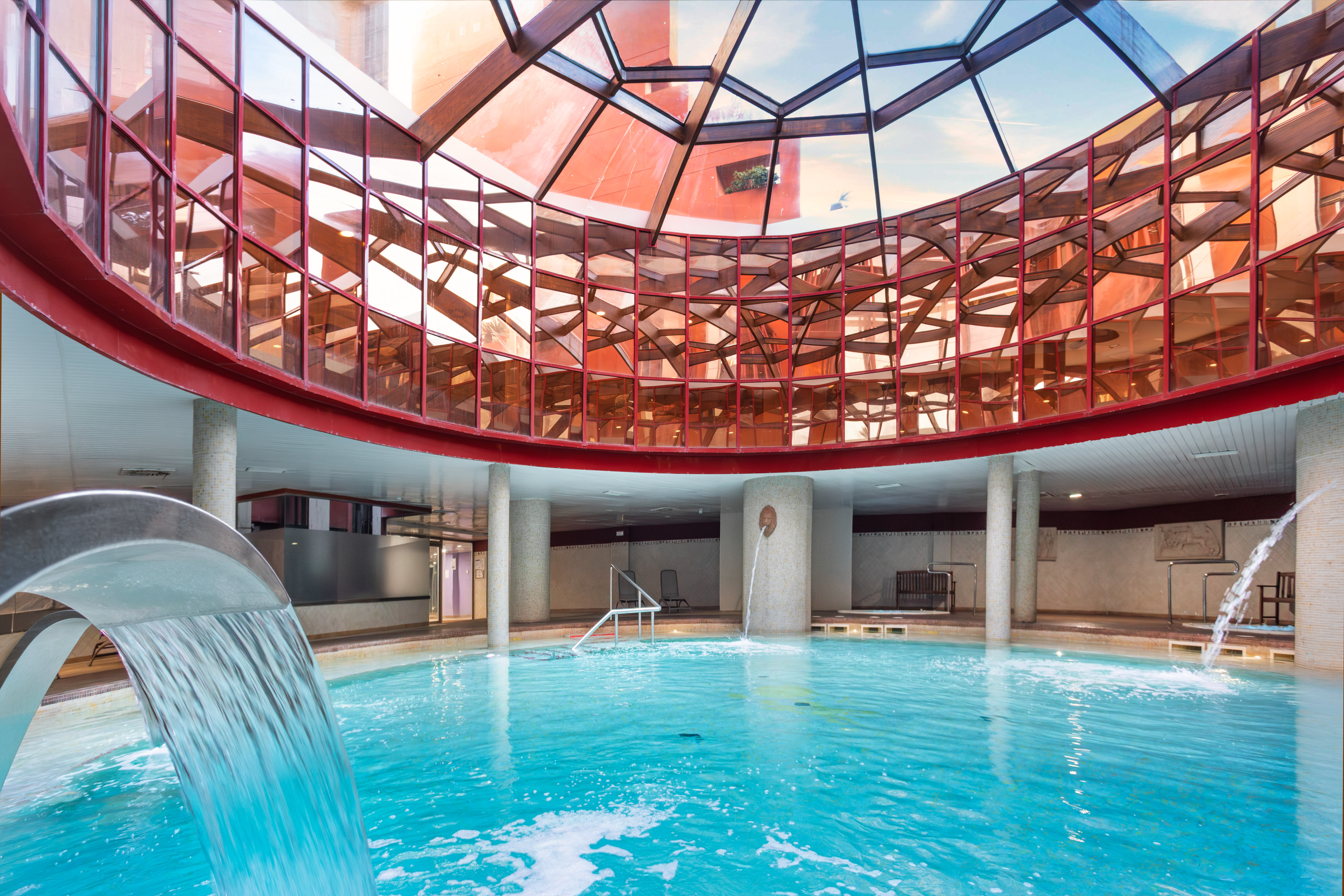 Indoor spa pool with curved glass ceiling, waterfall, and active water jets.