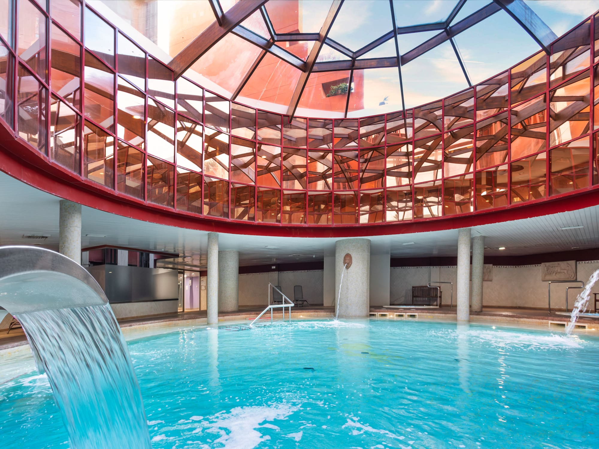 Indoor spa pool with curved glass ceiling, waterfall, and active water jets.