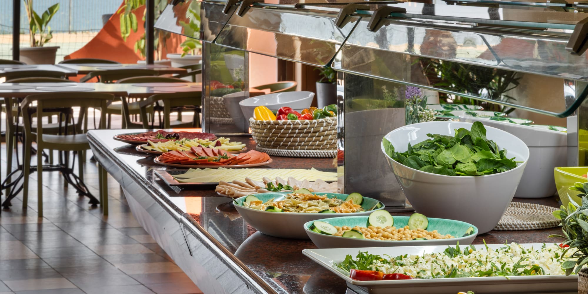 Hotel buffet with diverse salads, cold cuts, pasta, and sea view.