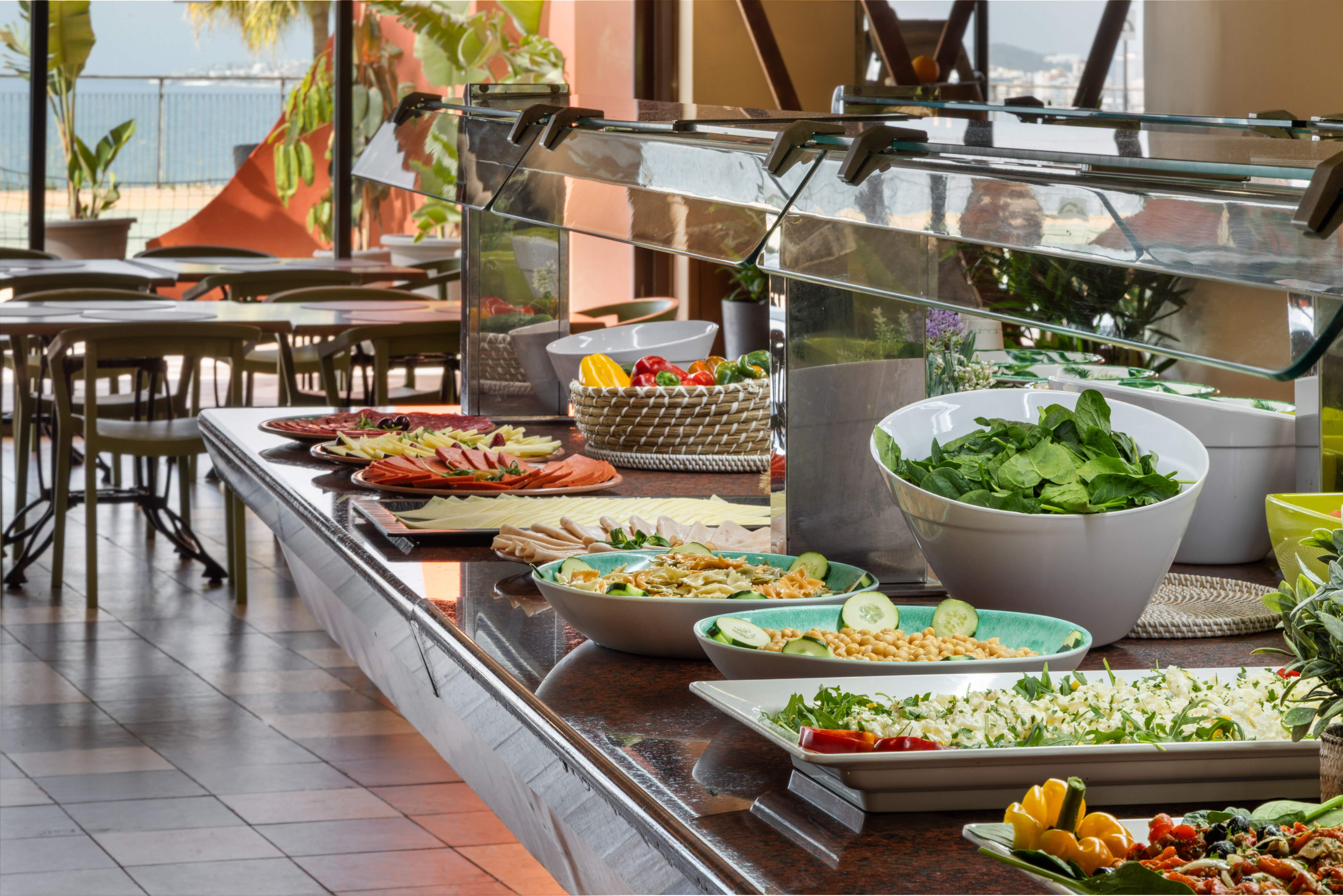 Hotel buffet with diverse salads, cold cuts, pasta, and sea view.
