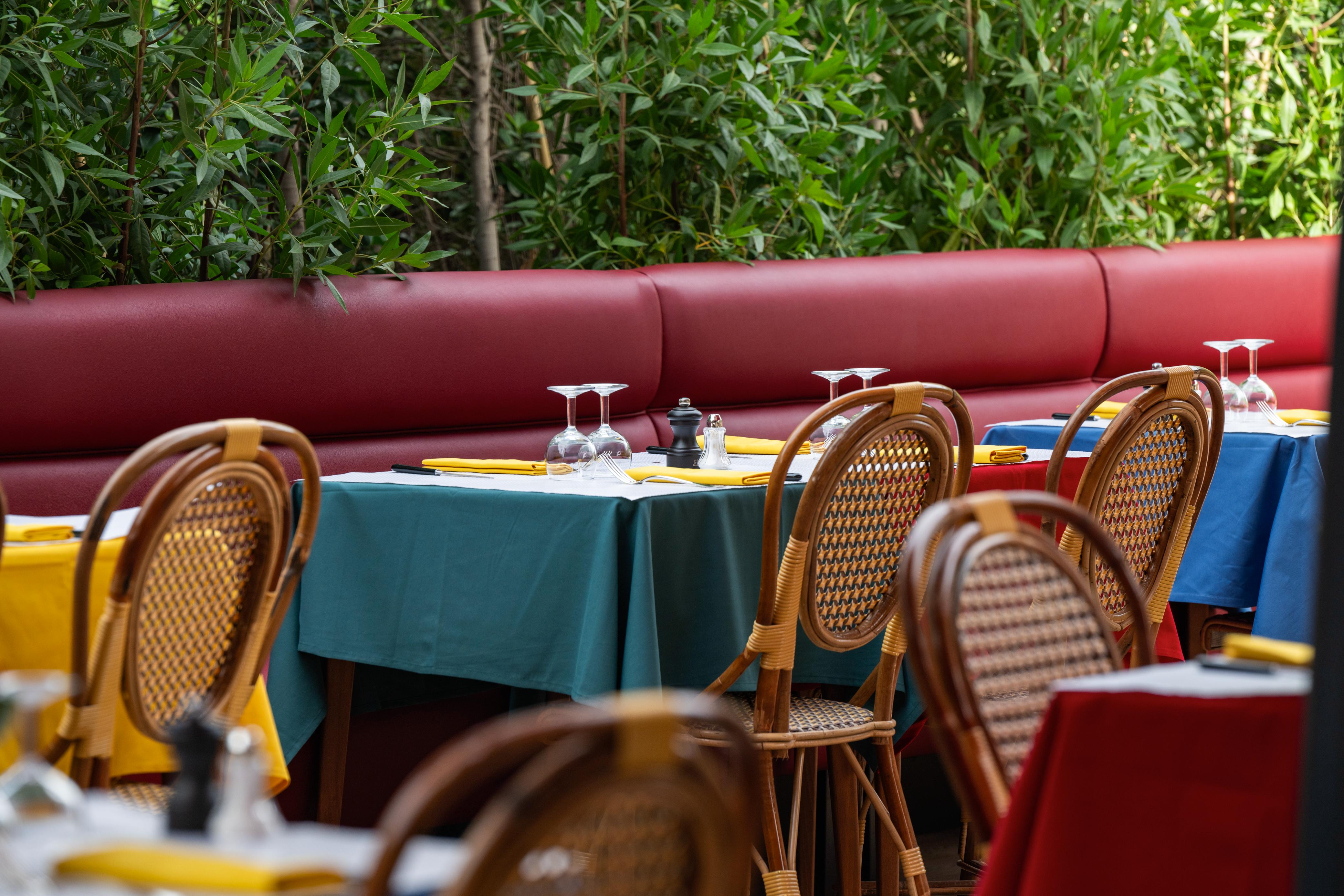 Colorful restaurant dining tables, bistro chairs, red booth, and green plants.