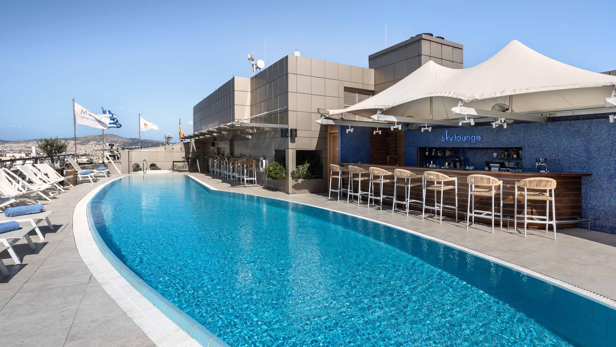 Bright rooftop pool and Sky Lounge bar with sun loungers and city skyline.