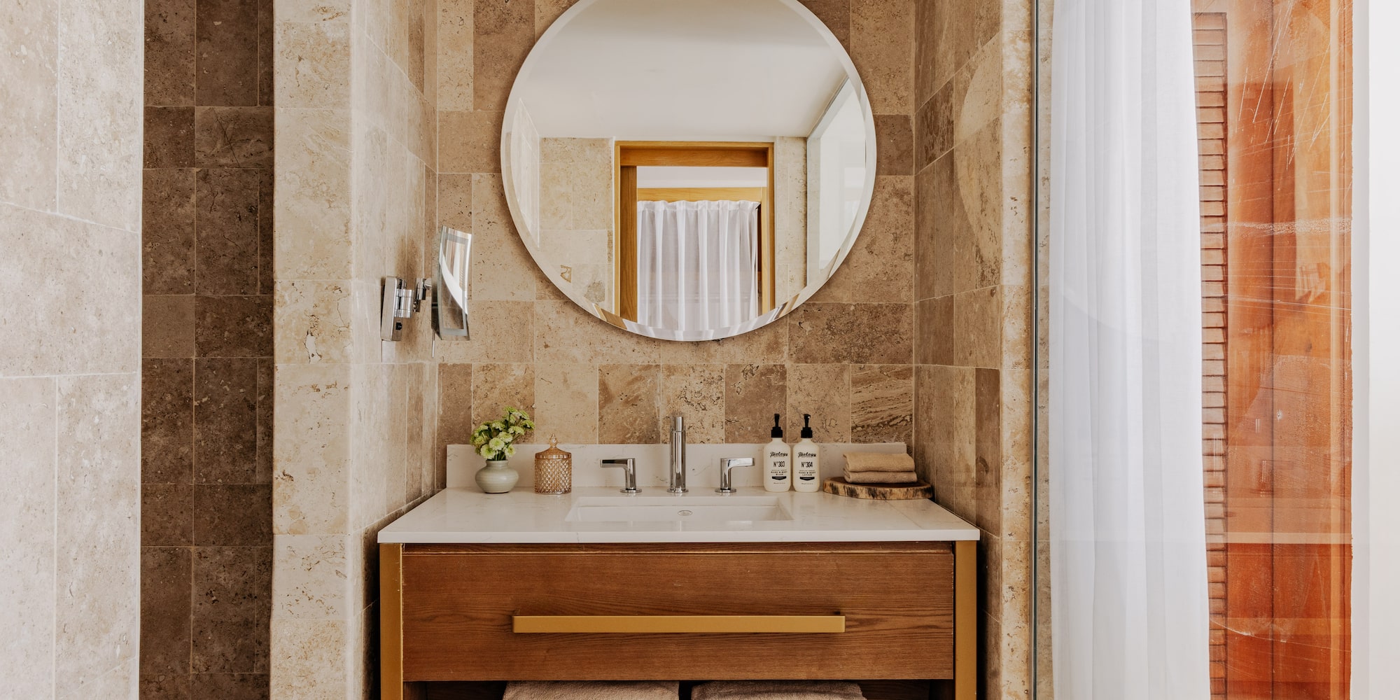 Modern bathroom vanity with sink, wood cabinet, round mirror, stone tiles.