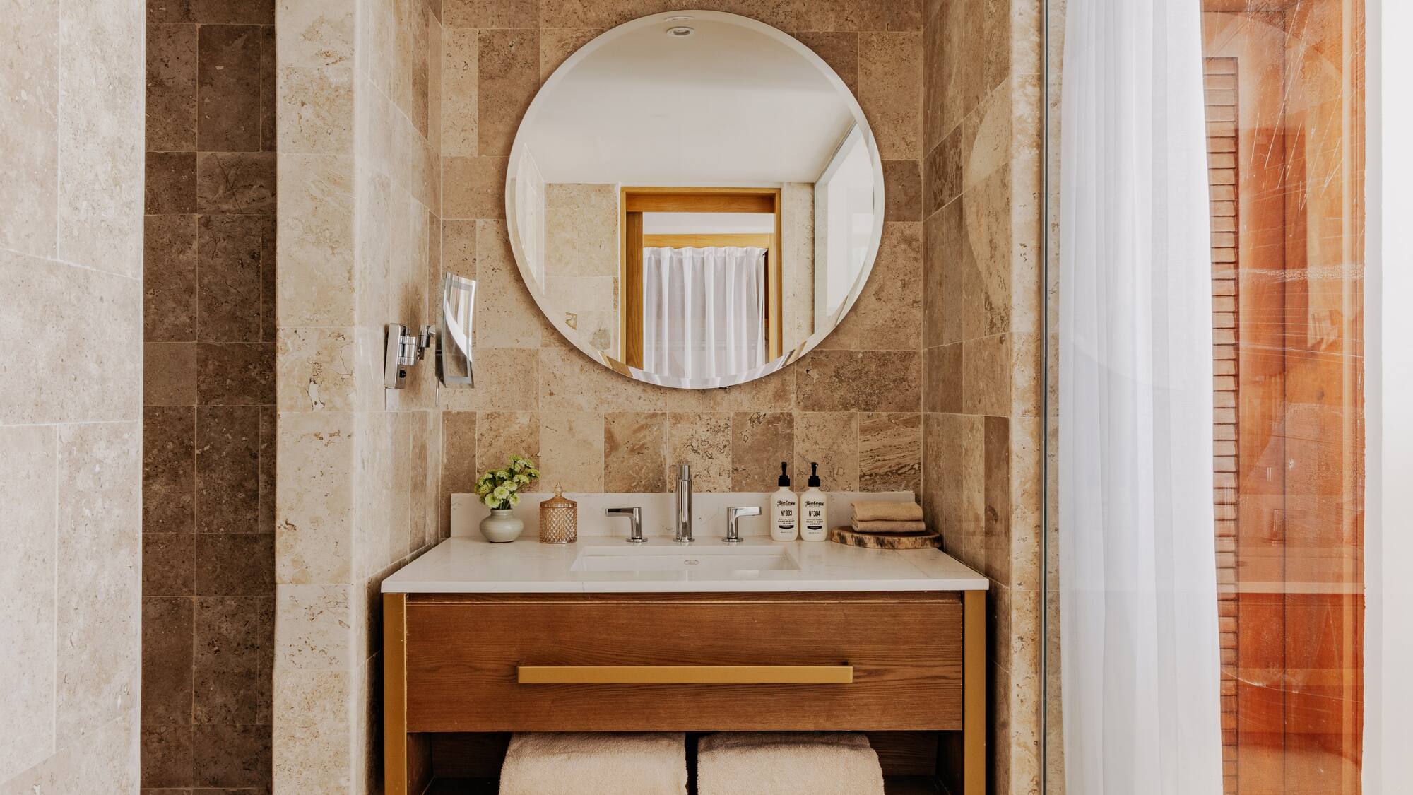 Modern bathroom vanity with sink, wood cabinet, round mirror, stone tiles.