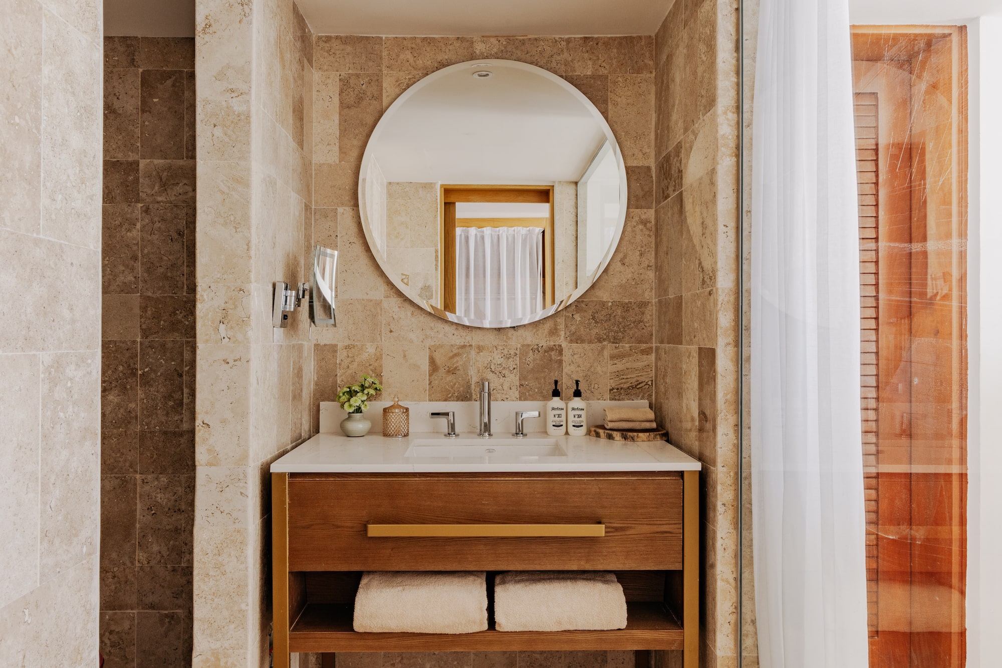 Modern bathroom vanity with sink, wood cabinet, round mirror, stone tiles.
