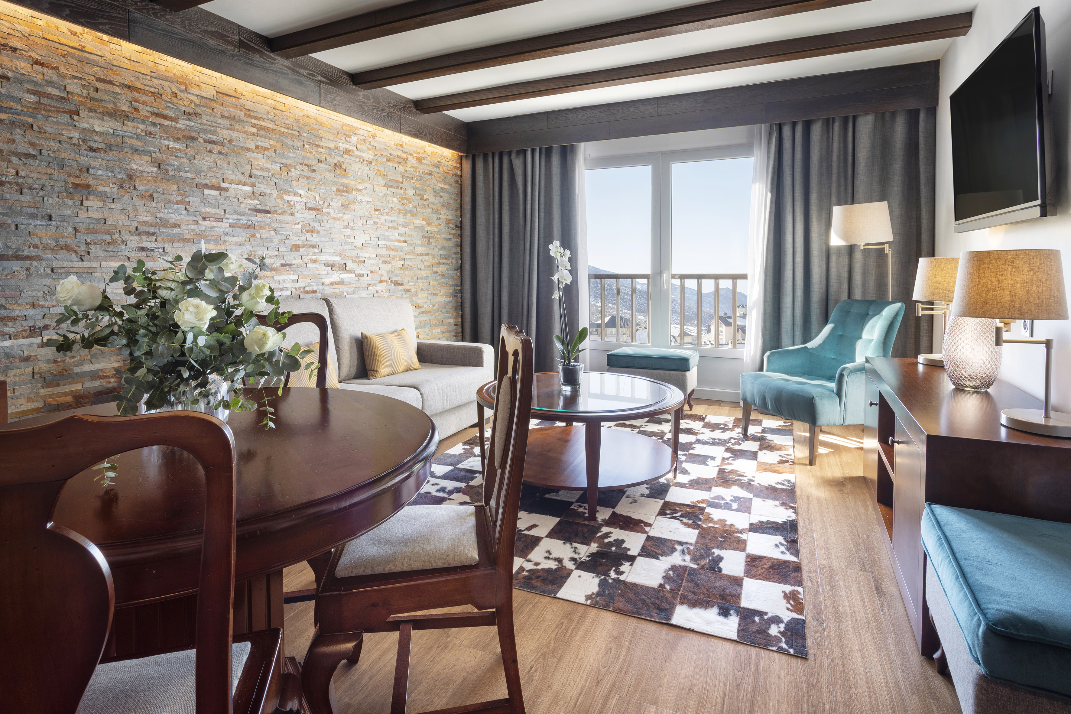 Hotel suite living room with stone wall, wooden beams, and mountain view.