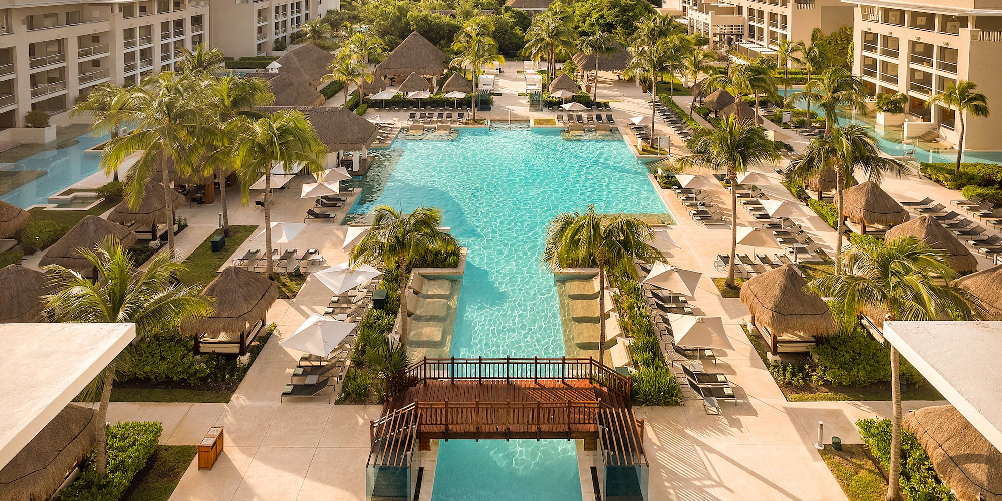 Tropical resort with multiple pools, palm trees, hotel, and ocean.