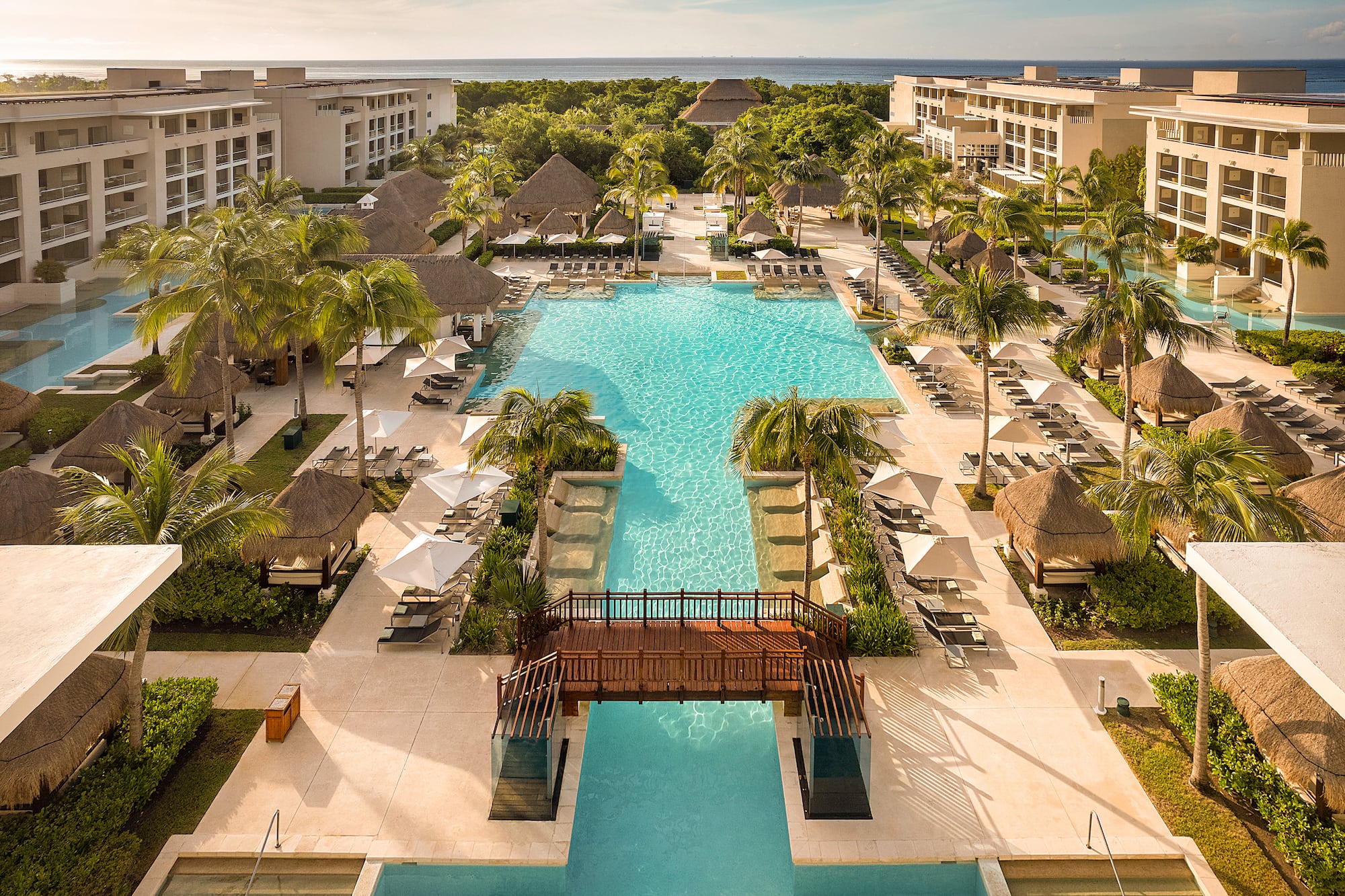 Tropical resort with multiple pools, palm trees, hotel, and ocean.