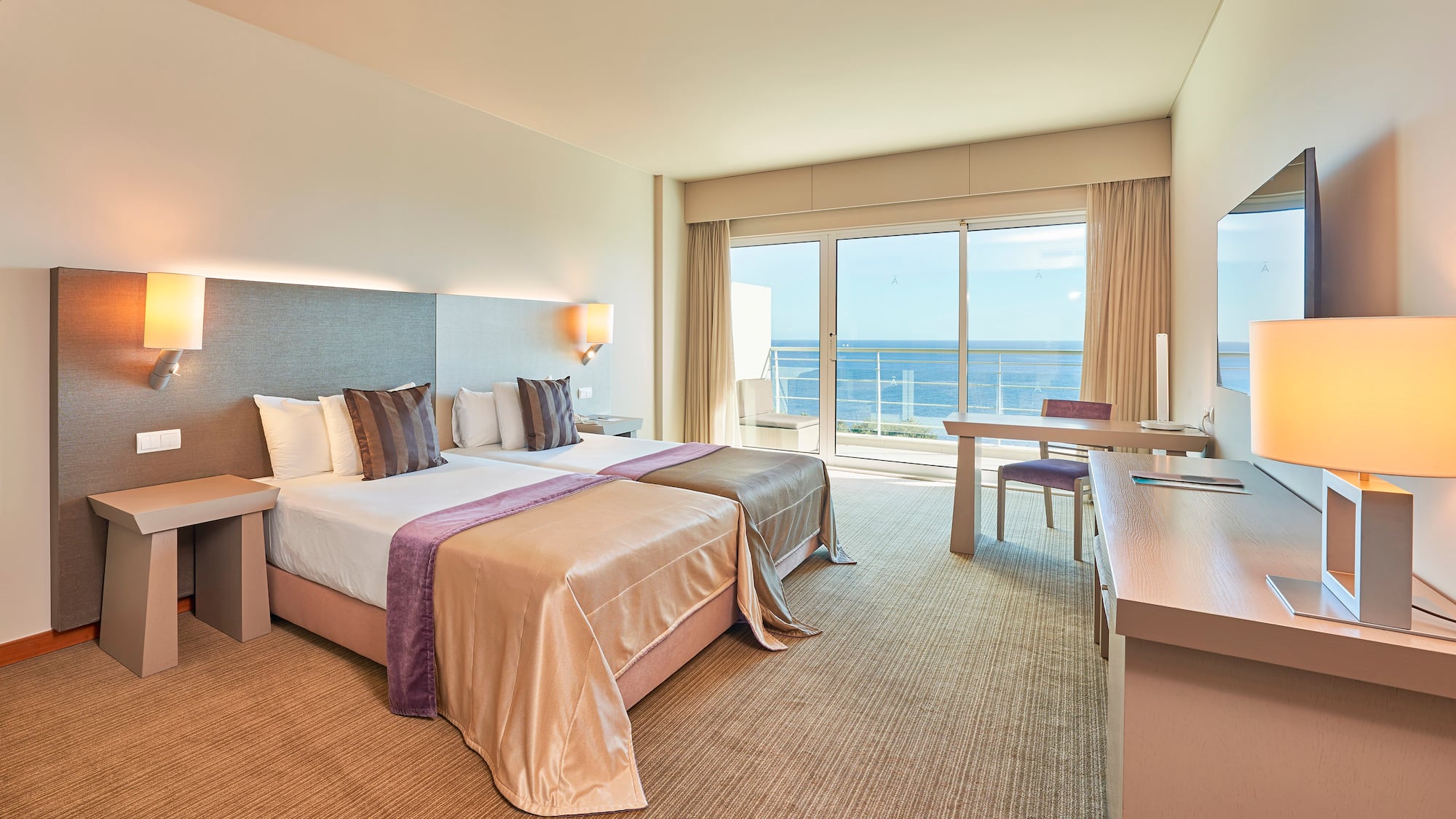 Modern hotel room with twin beds and ocean view balcony.