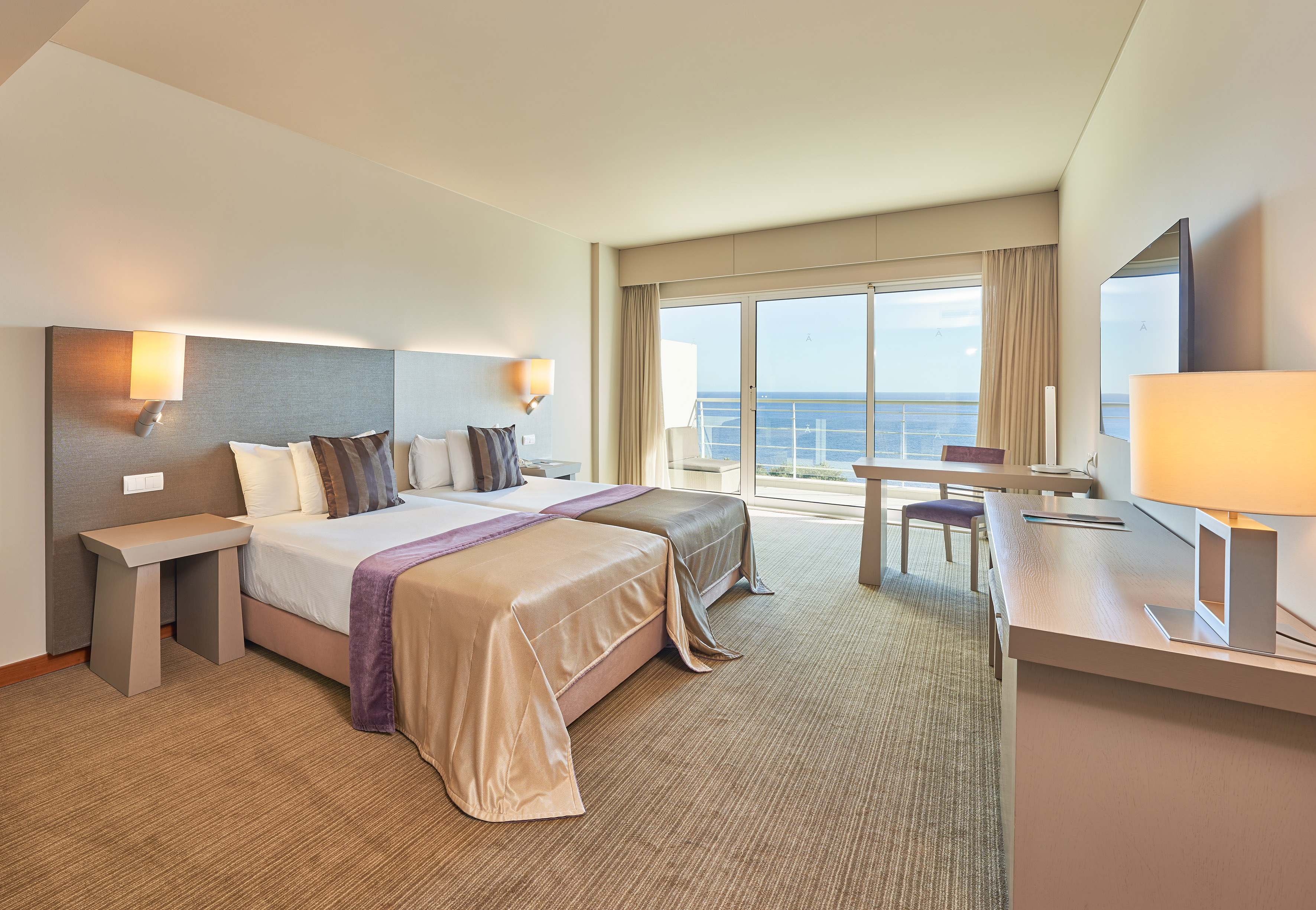 Modern hotel room with twin beds and ocean view balcony.