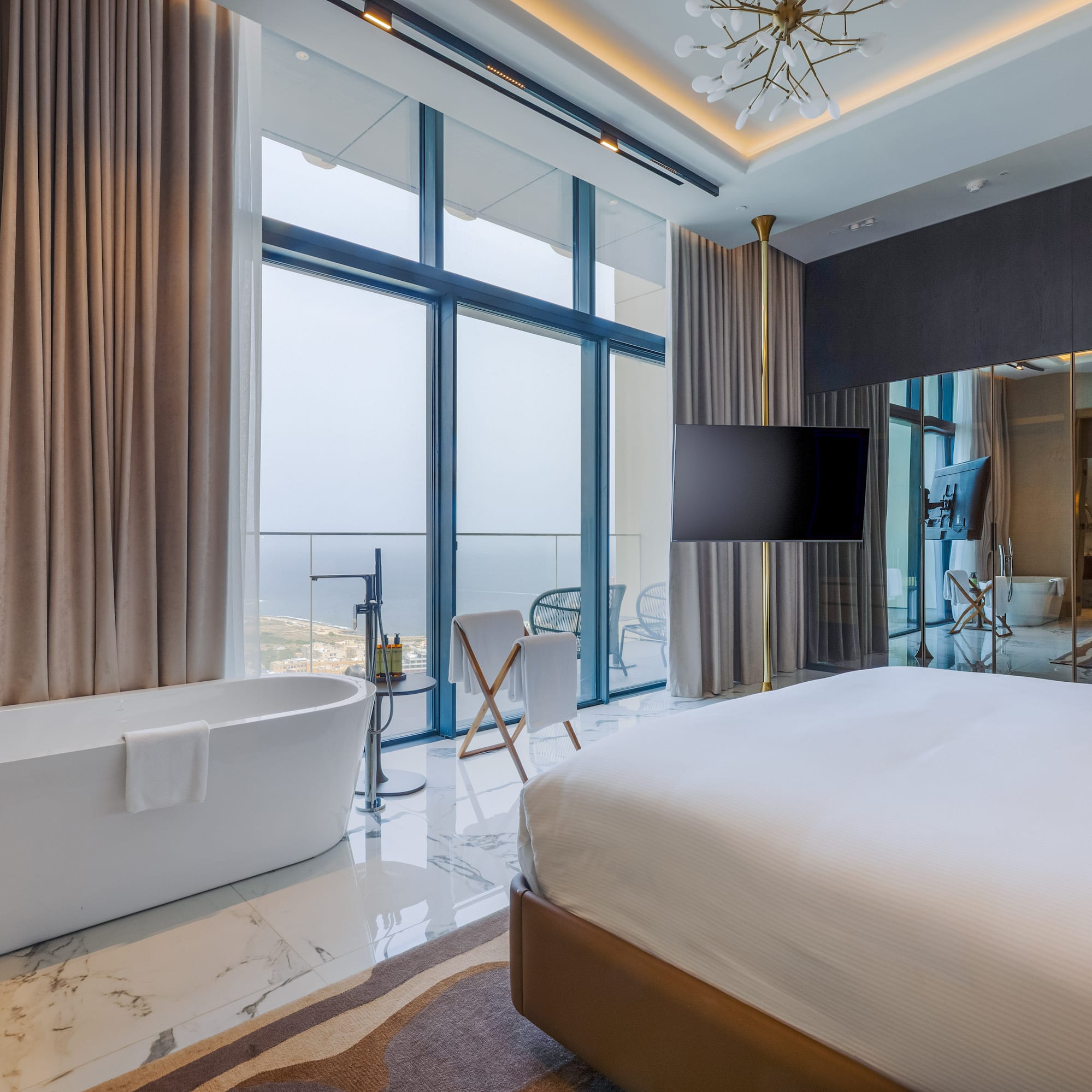 Modern hotel room with freestanding bathtub, king bed, and cityscape view.