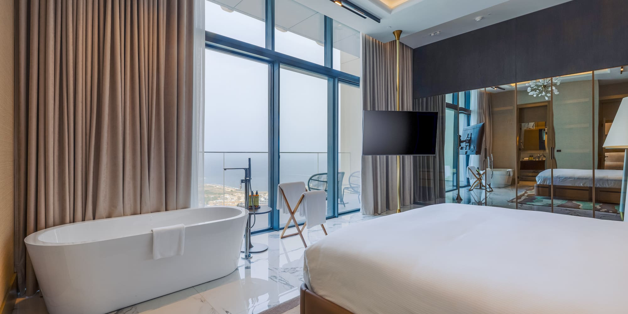 Modern hotel room with freestanding bathtub, king bed, and cityscape view.