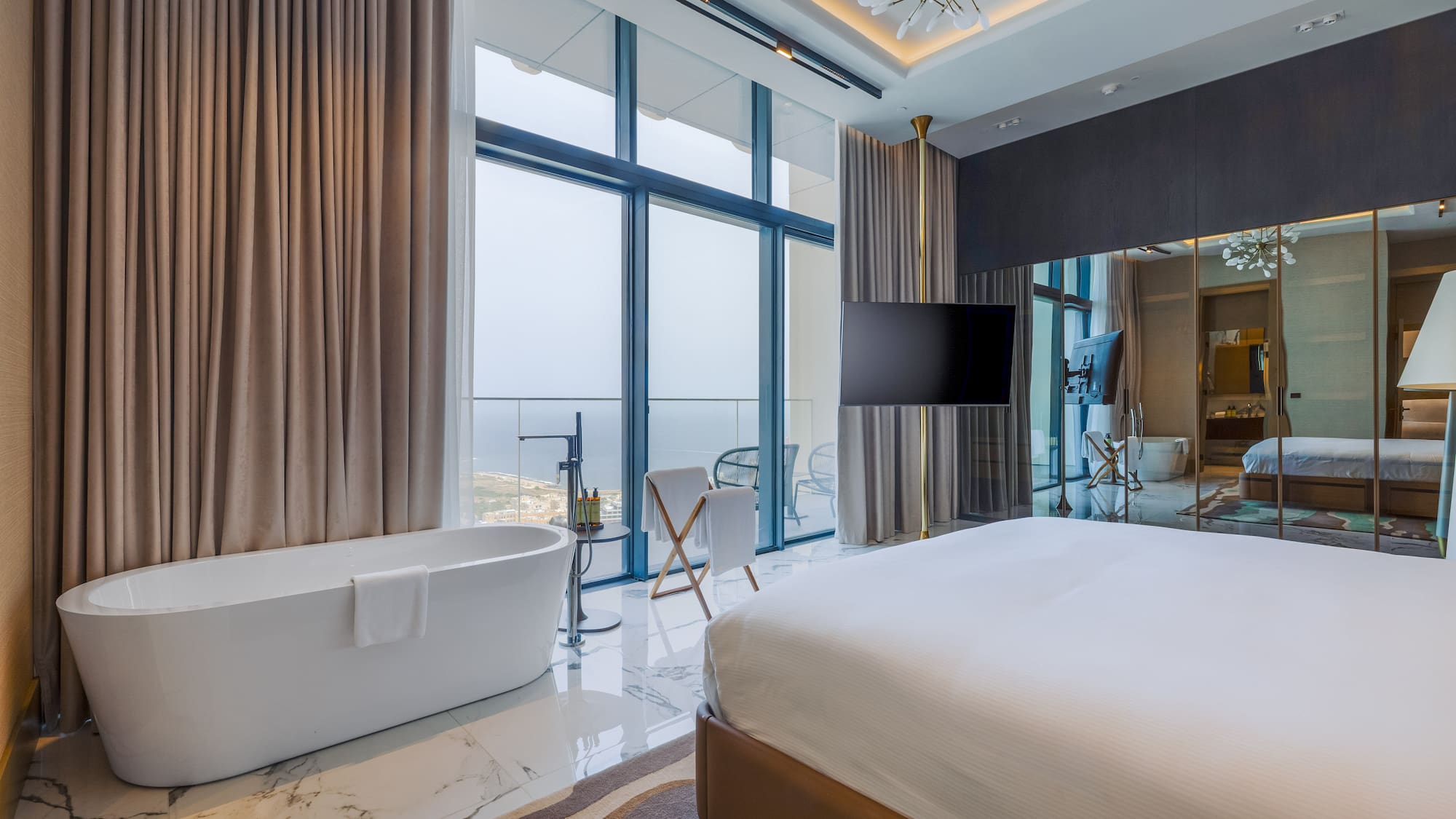Modern hotel room with freestanding bathtub, king bed, and cityscape view.
