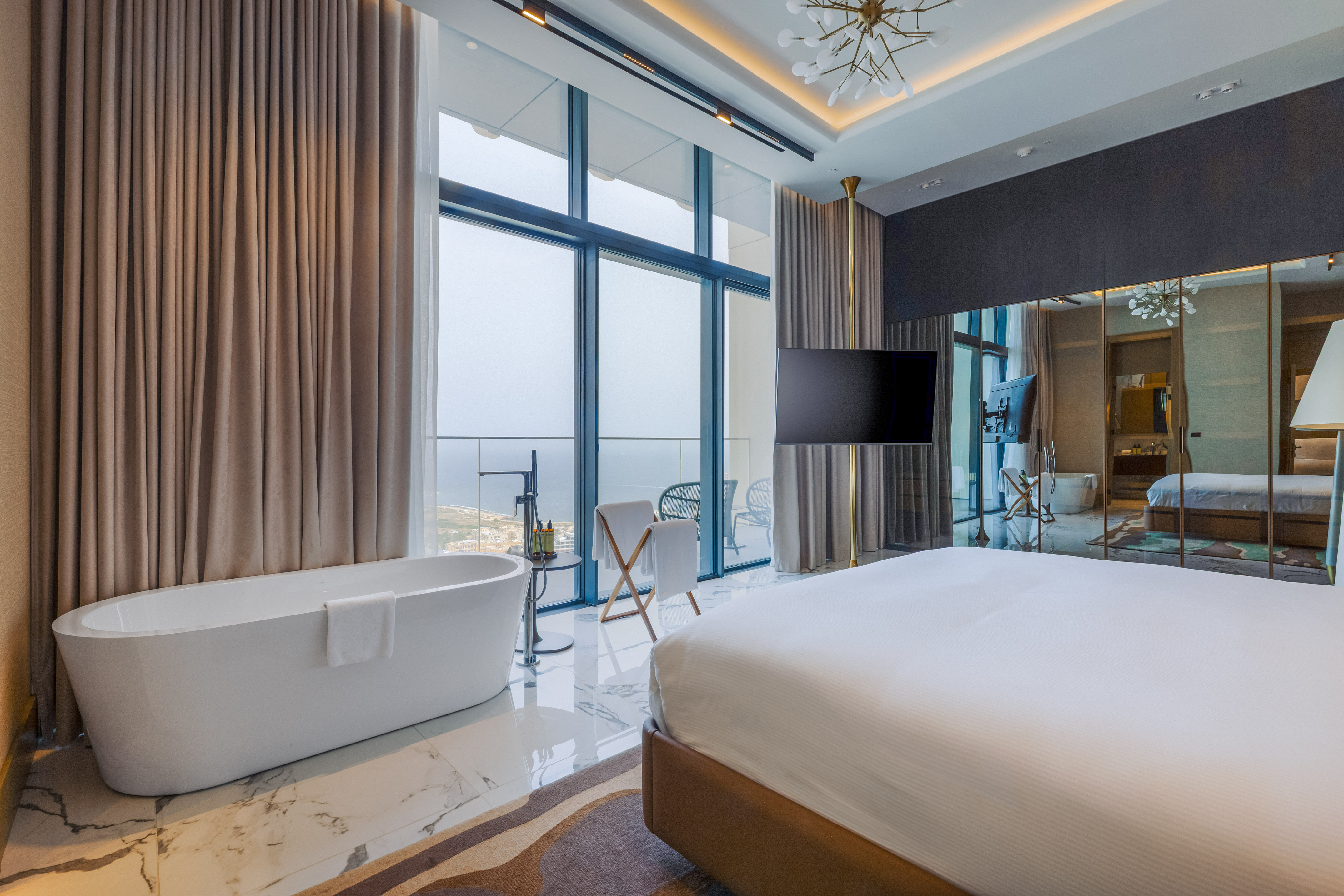 Modern hotel room with freestanding bathtub, king bed, and cityscape view.