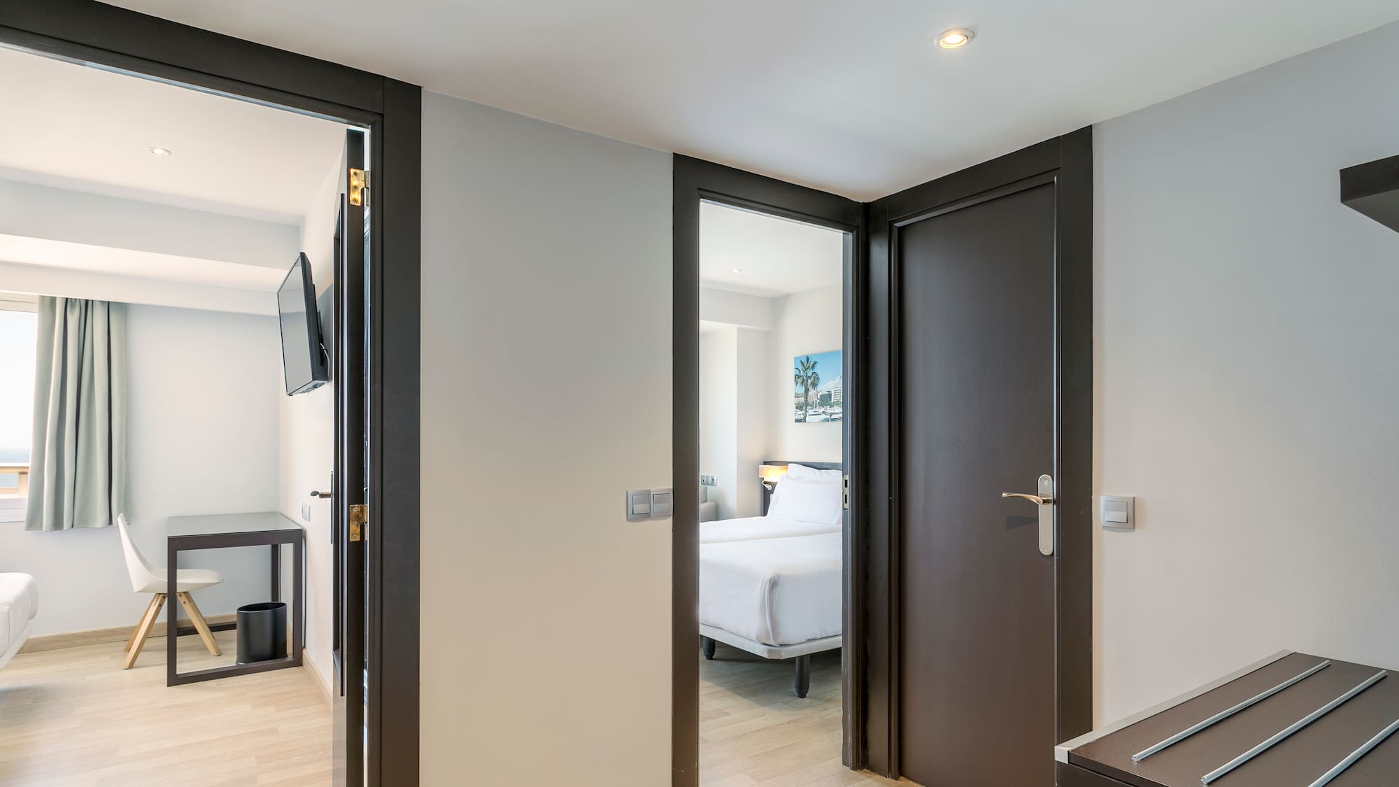 Bright hotel hallway showing two modern rooms: one with twin beds, one with desk.
