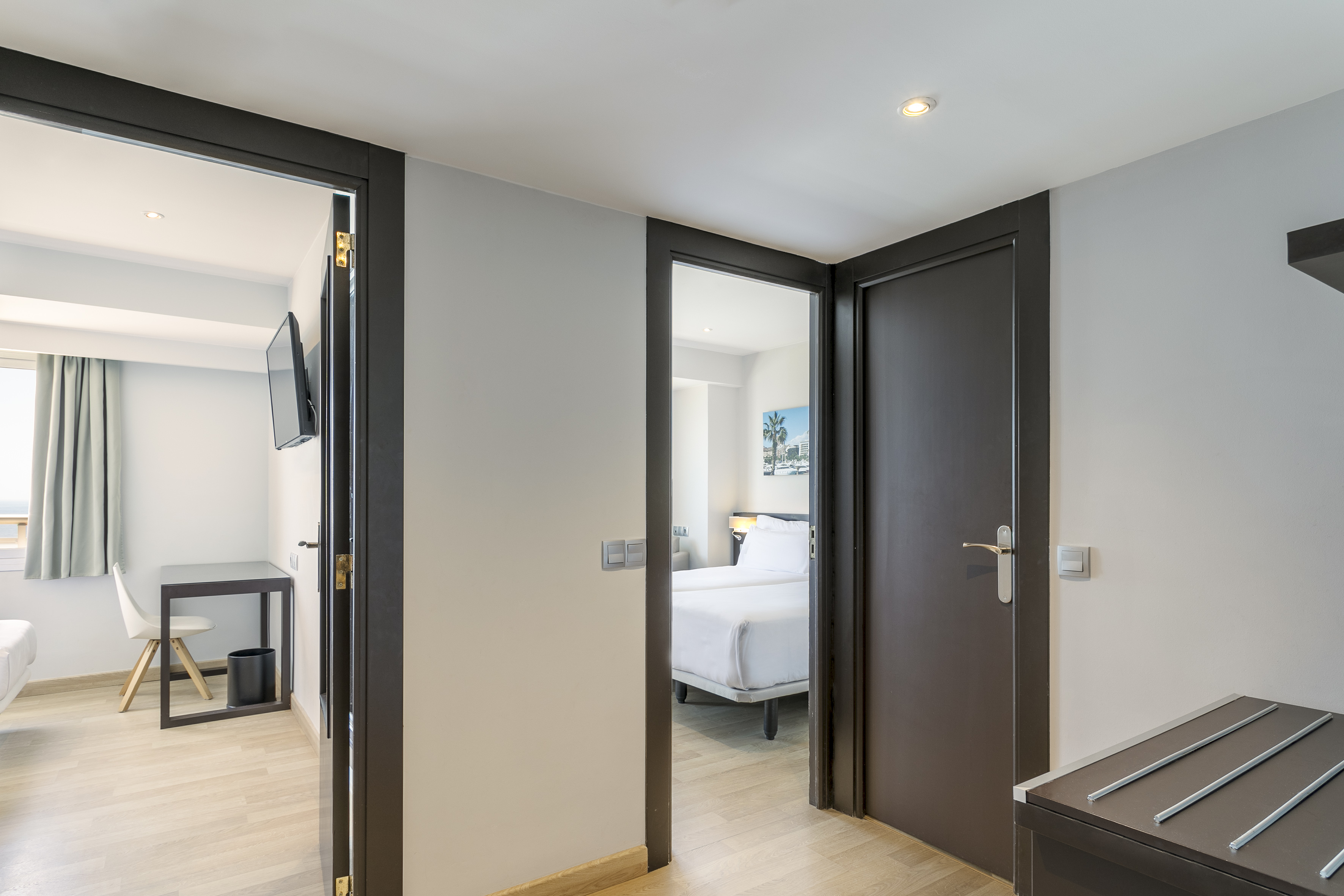 Bright hotel hallway showing two modern rooms: one with twin beds, one with desk.