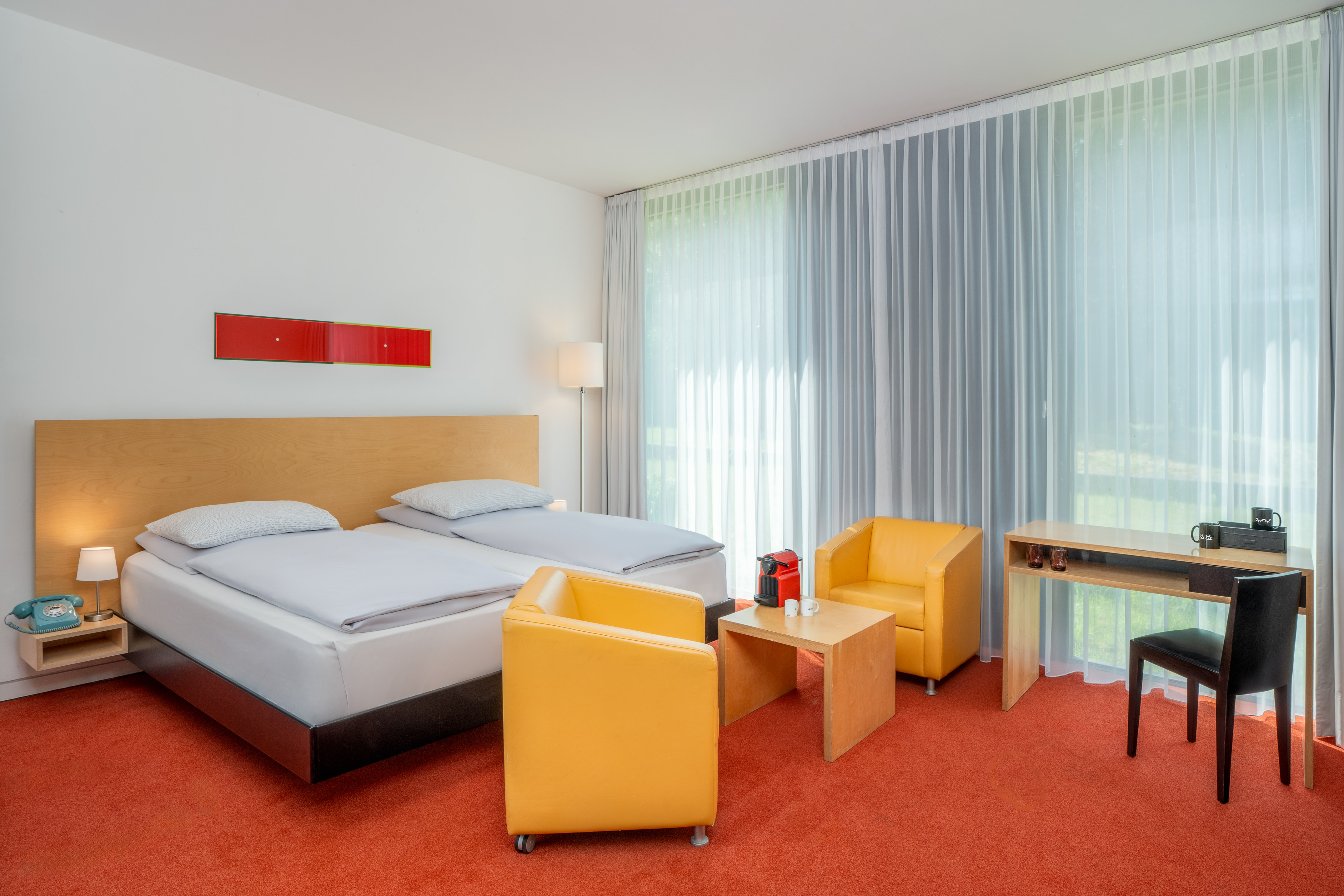 Modern hotel room with twin beds, orange carpet, yellow armchairs, and a desk. - The INNSiDE Premium Room - INNSiDE Düsseldorf Seestern, Düsseldorf