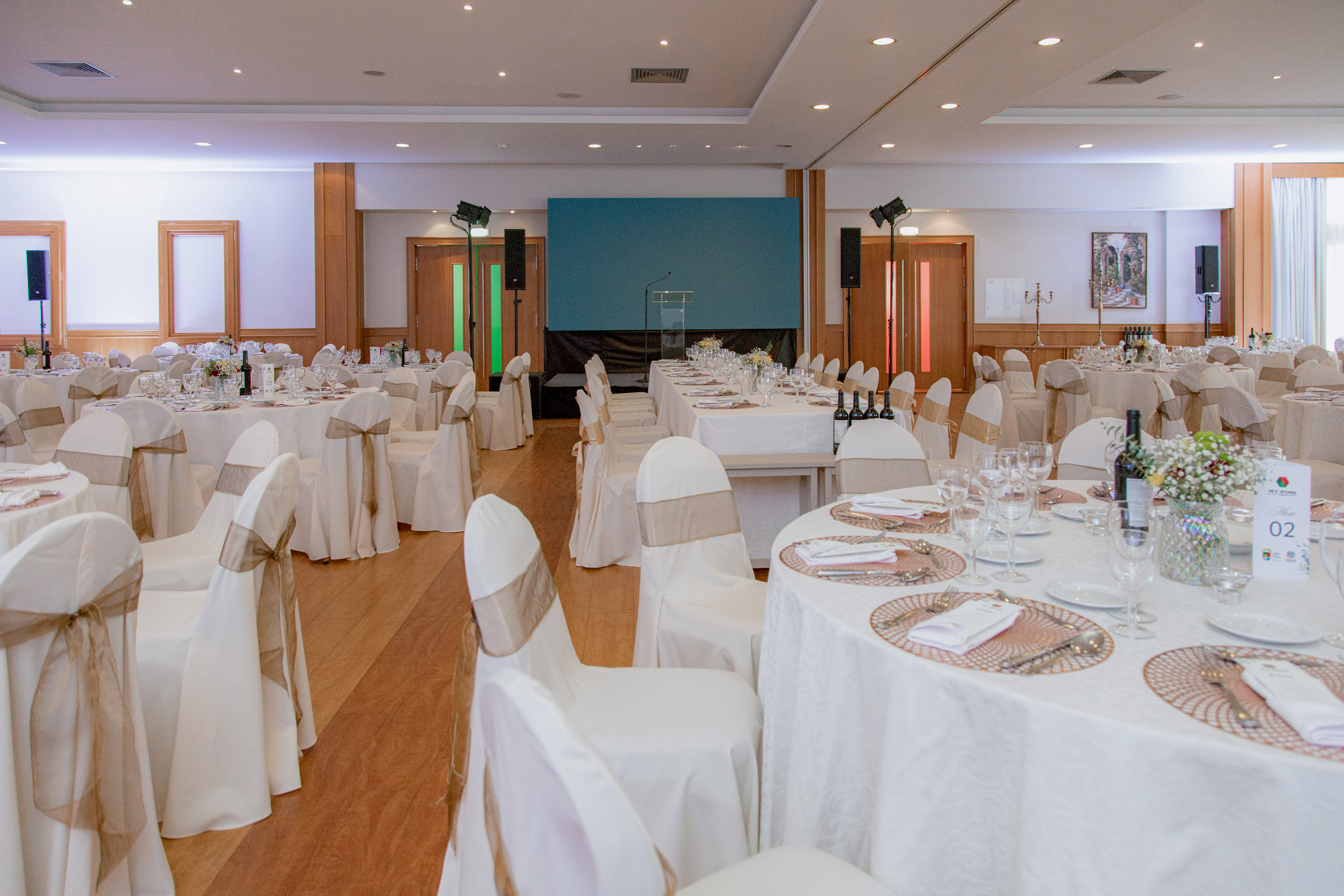 Elegant banquet hall with white tables, chairs with gold sashes, and stage setup.