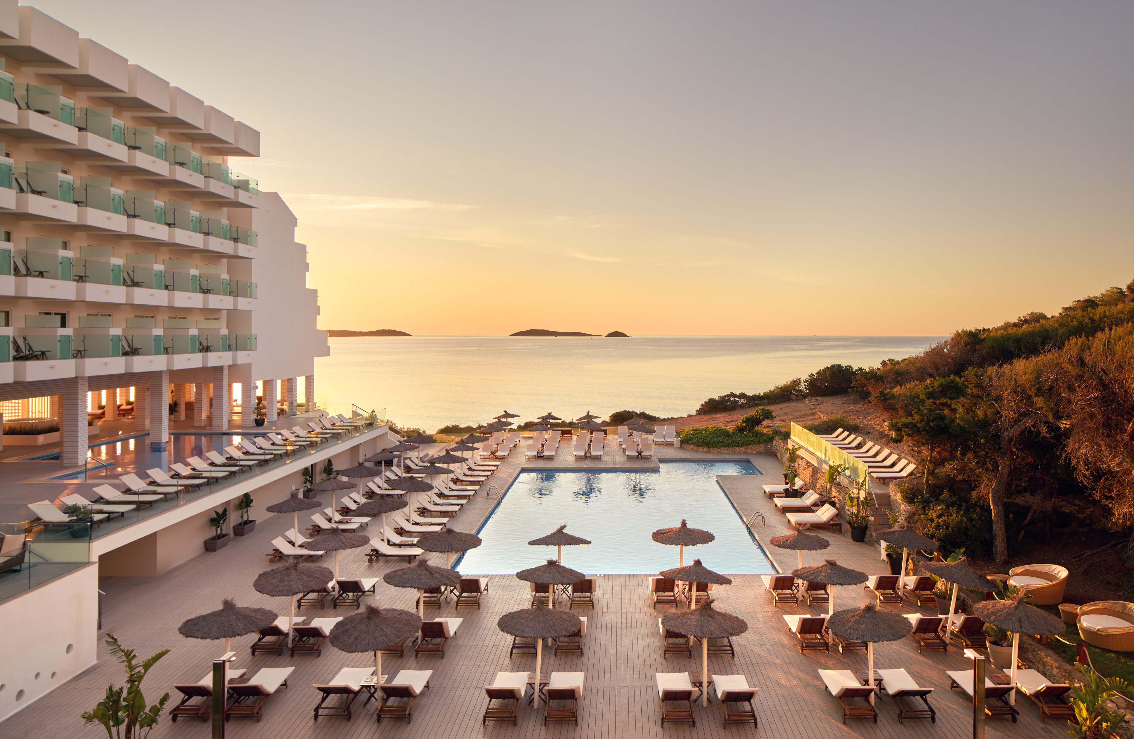Beachfront hotel with large swimming pool, loungers, and sea view at sunset.
