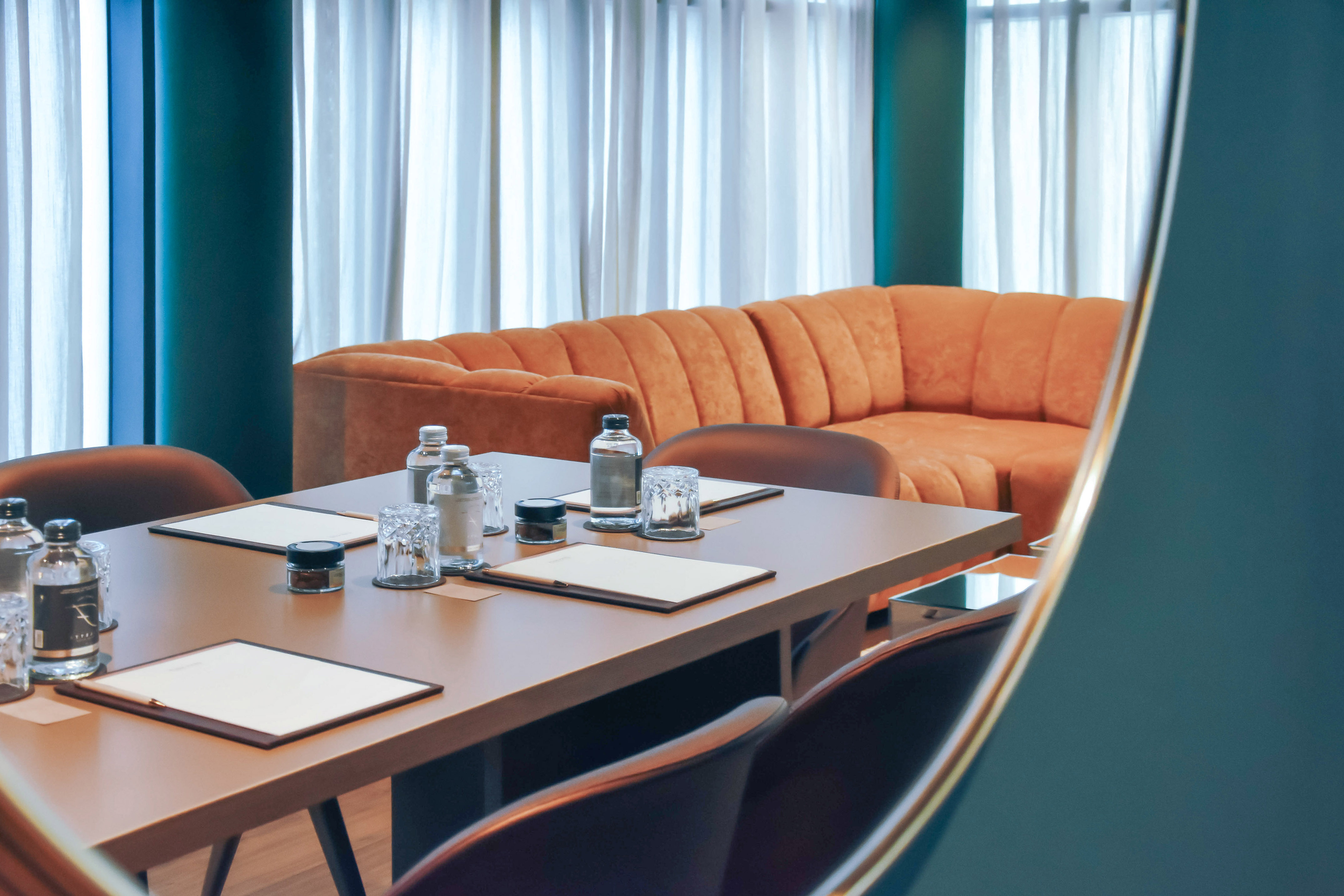 Stylish conference room with orange sofa, wooden table, and teal decor.