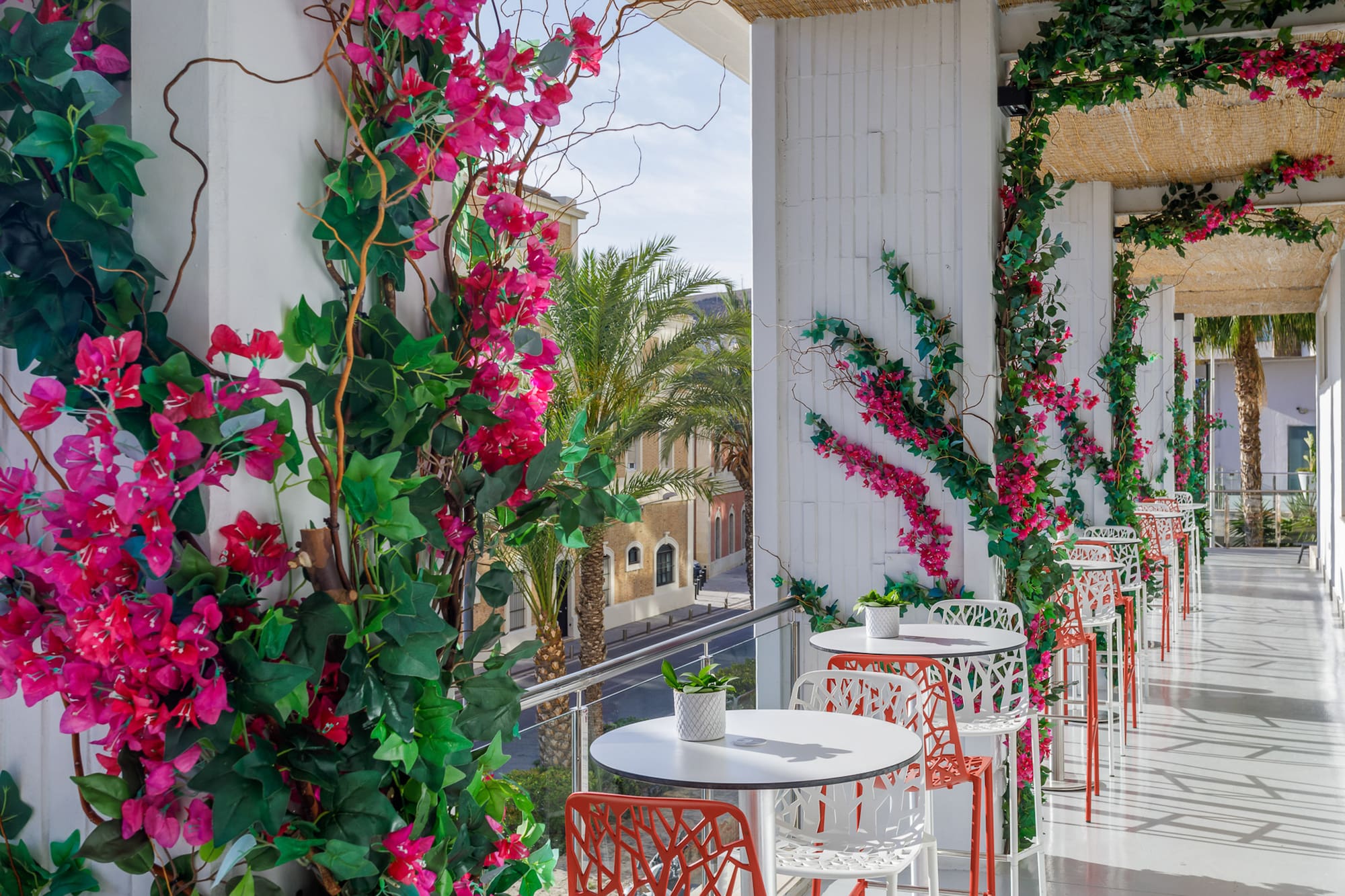 Vibrant pink bougainvillea on a sunny outdoor cafe balcony with tables and city view.