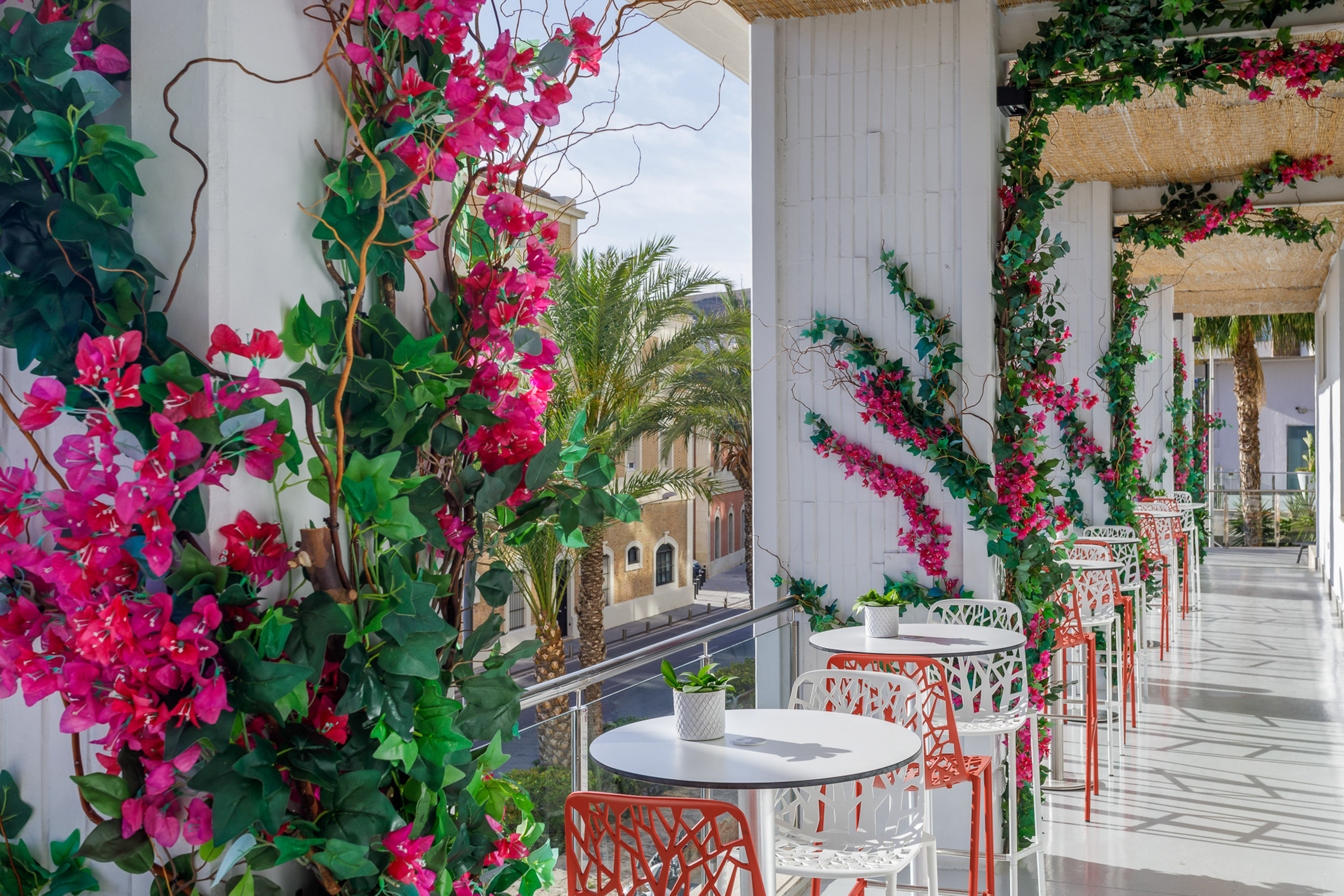 Vibrant pink bougainvillea on a sunny outdoor cafe balcony with tables and city view.