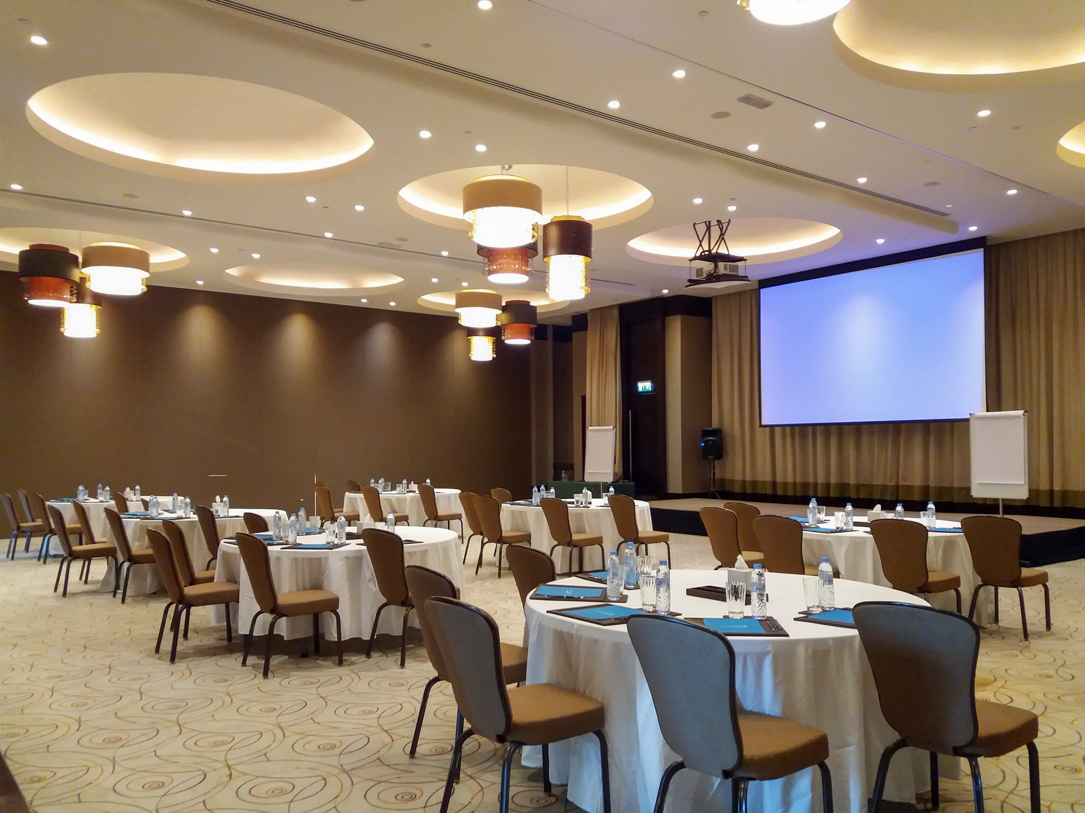Modern conference room with round tables, chairs, and large projector screen.