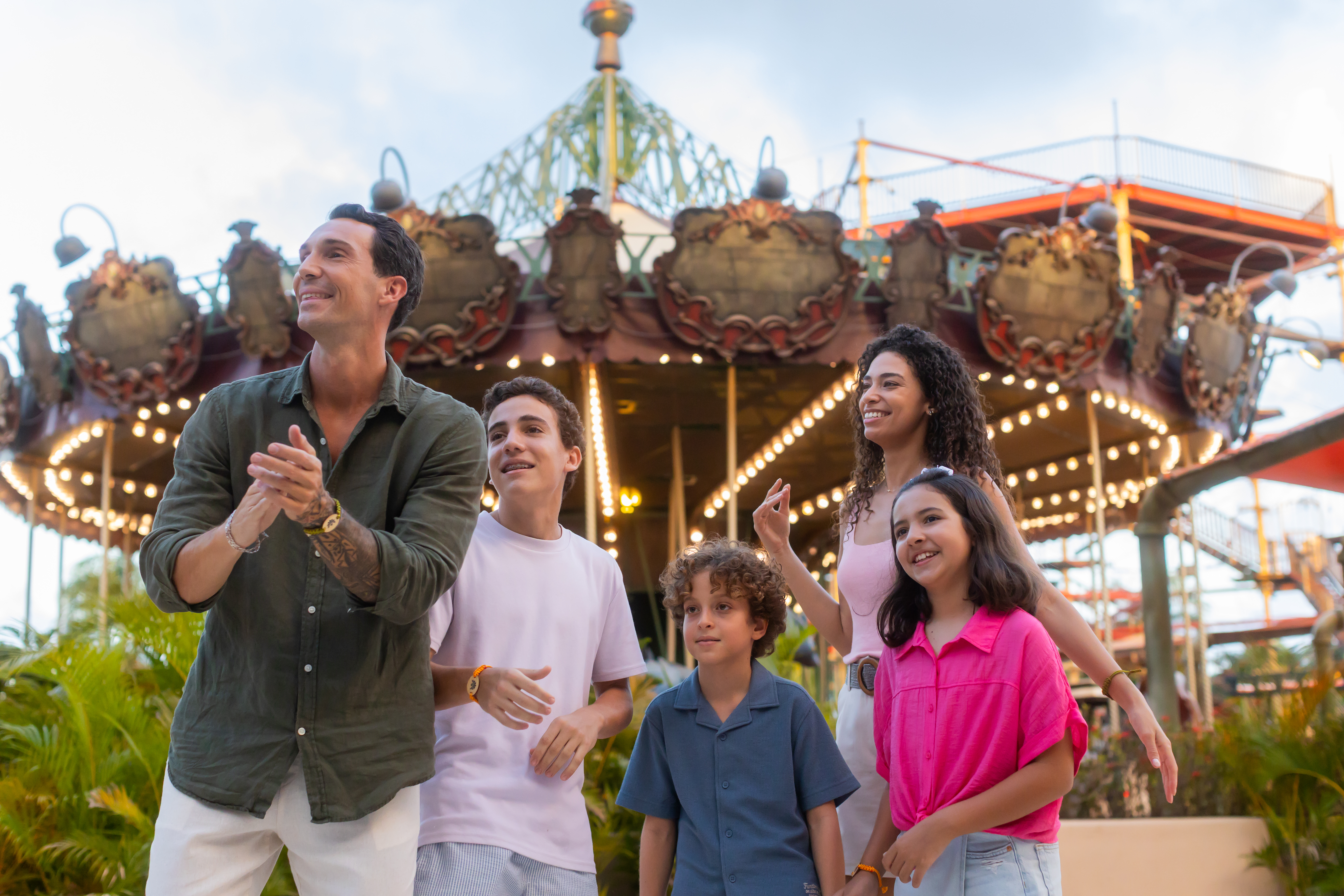 Happy family with three kids enjoying amusement park, bright carousel in background.