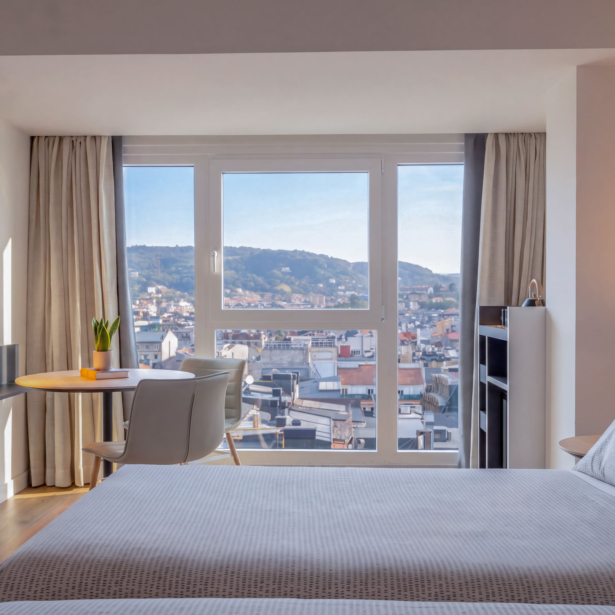 Dormitorio de hotel moderno con cama, escritorio y vista panorámica a la ciudad.