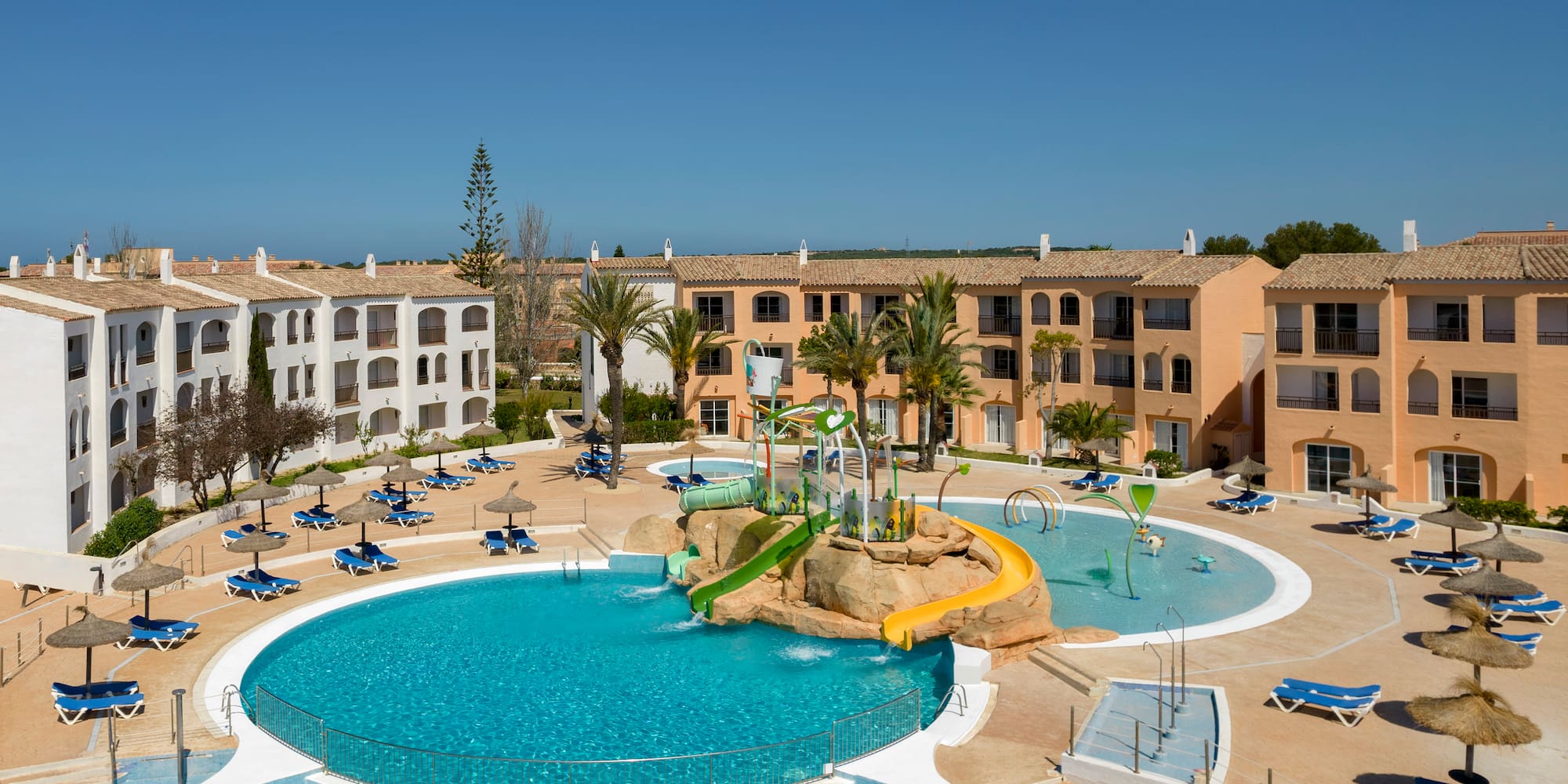Resort outdoor pool with water slides, sun loungers, and hotel apartments.