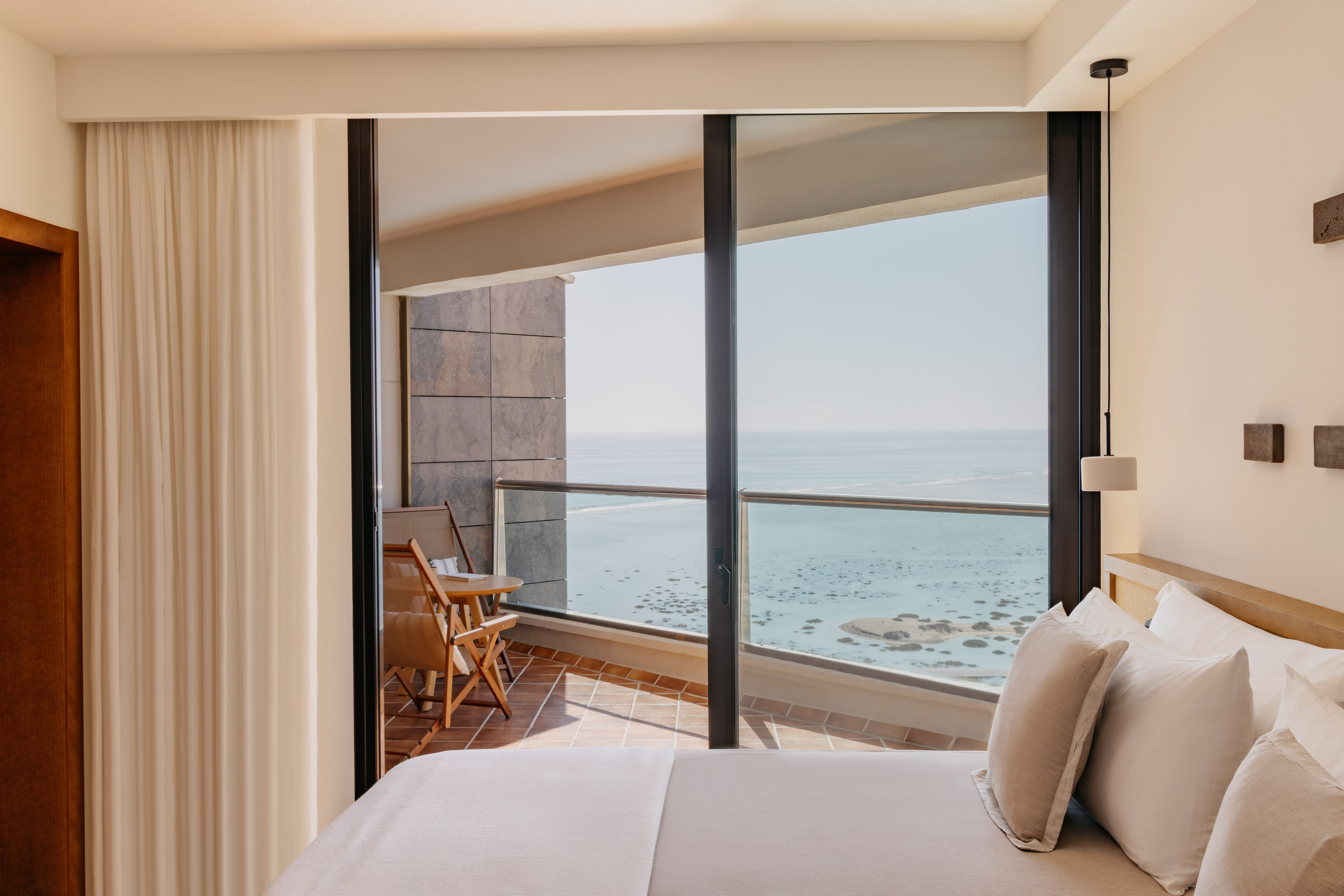 Modern hotel room with ocean view balcony and outdoor seating.