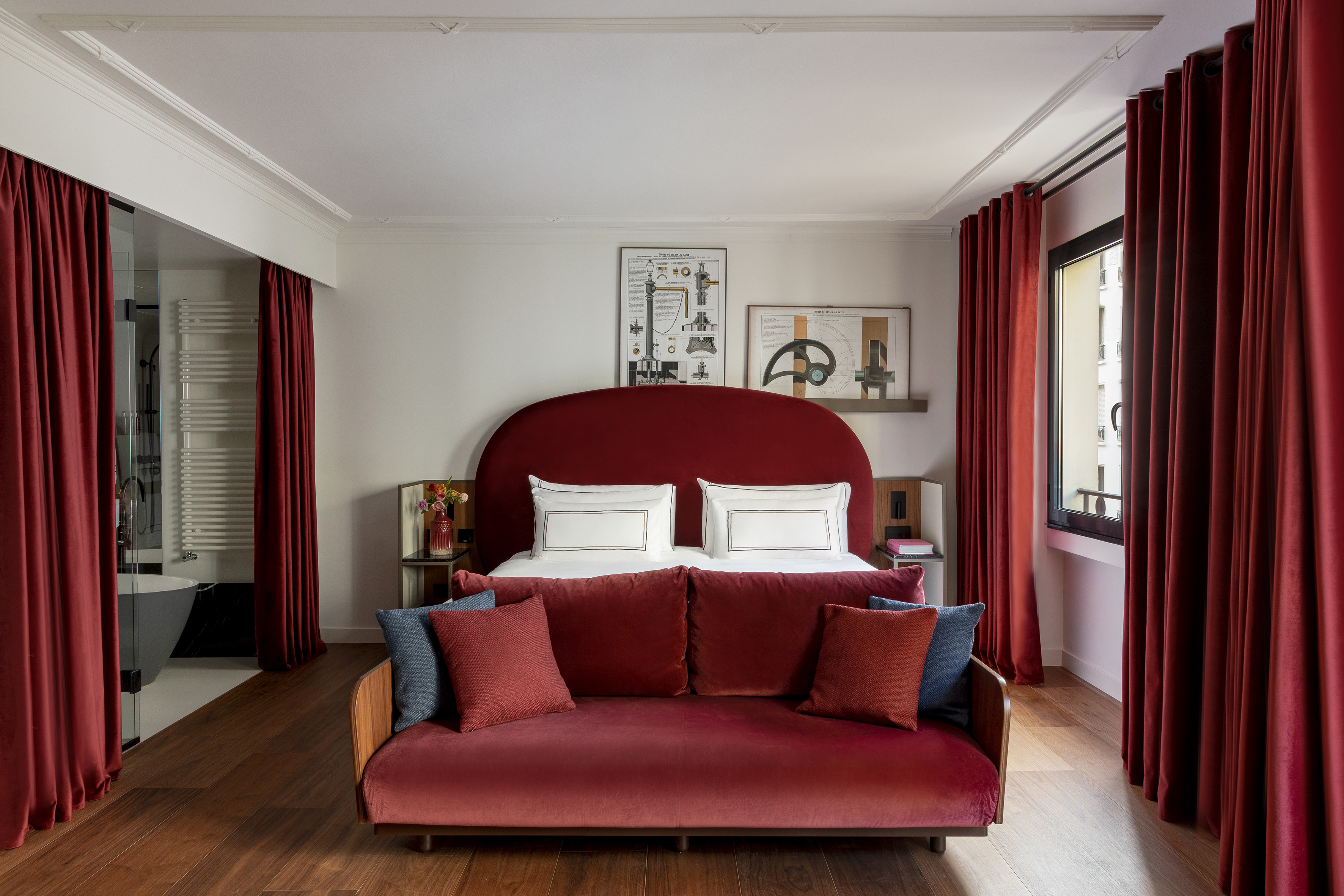 Red velvet luxury bedroom with bold headboard, sofa, and matching curtains.
