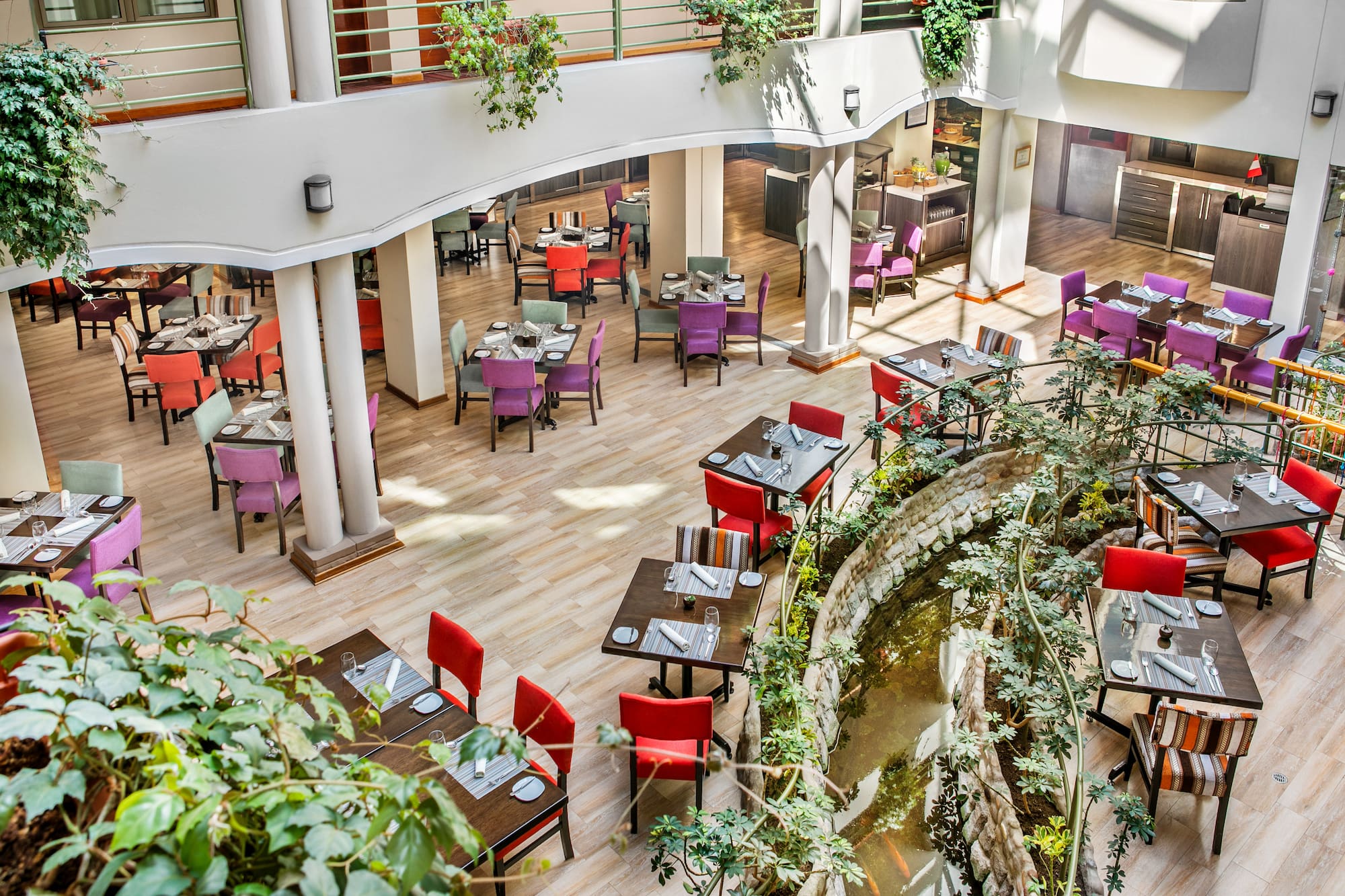 Colorful restaurant atrium with dining tables, chairs, plants, and pond. - Hotel Cusco La Paccha Affiliated by Meliá, Cusco