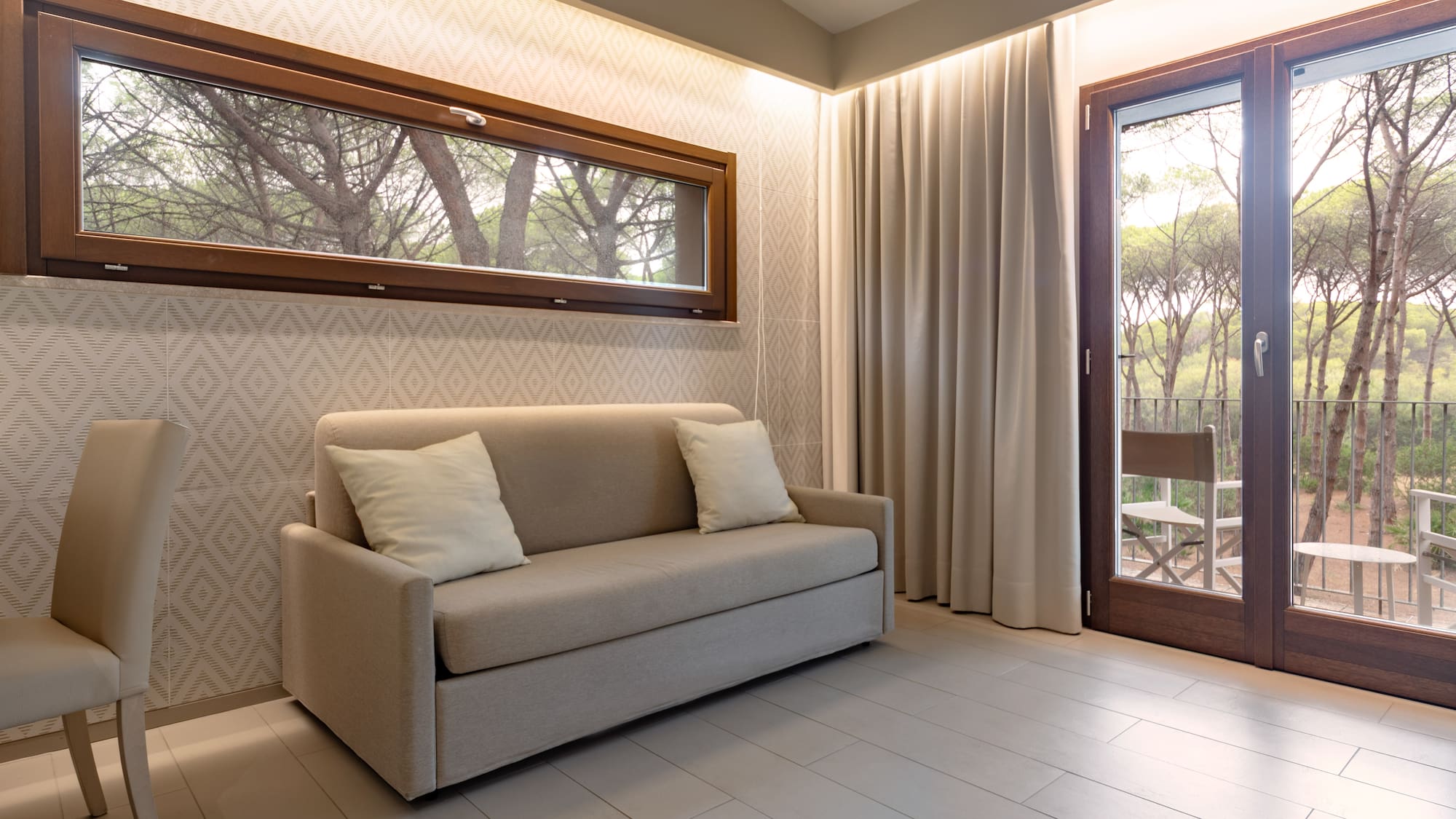 Modern hotel room with sofa bed, forest view balcony, and large window.
