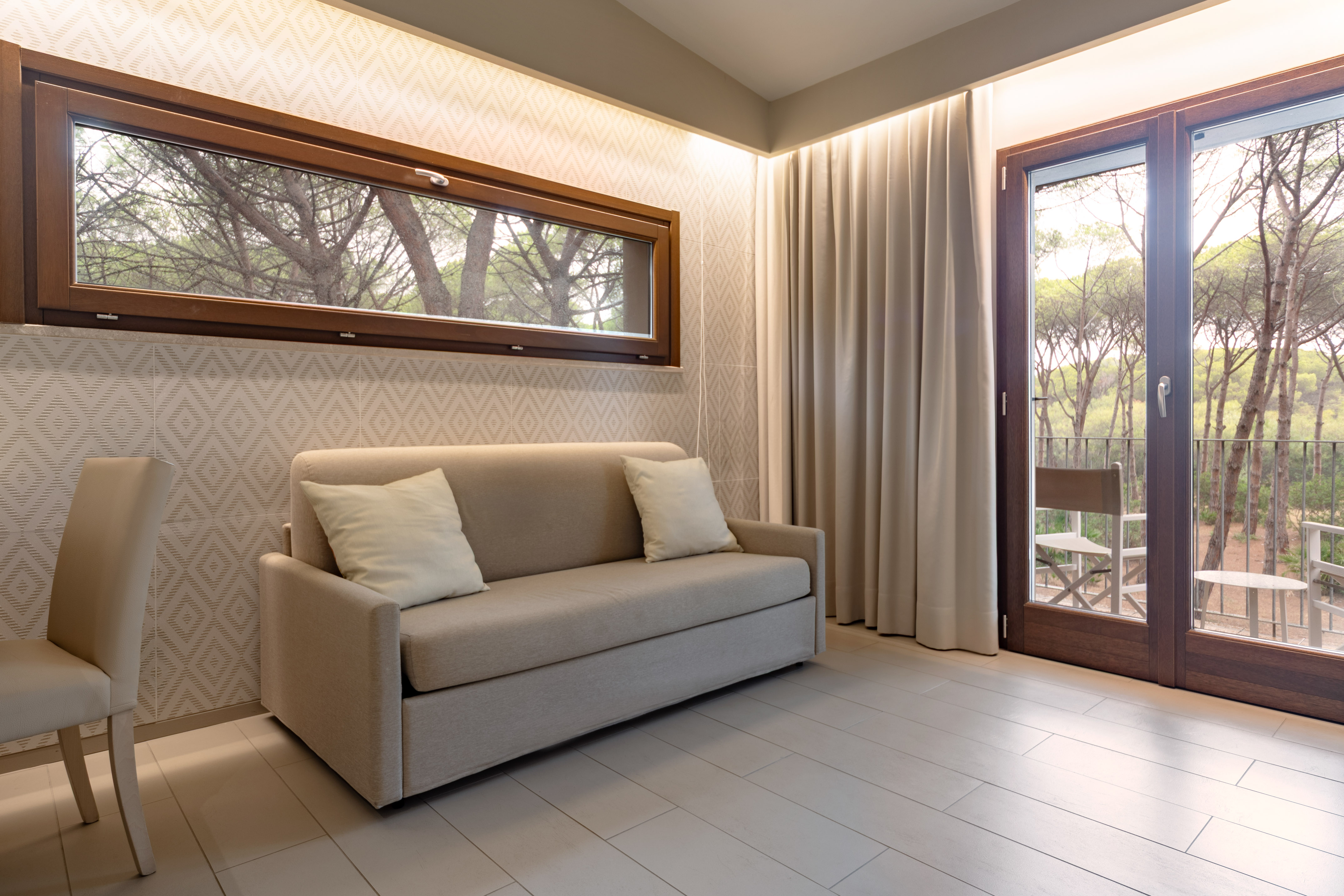 Modern hotel room with sofa bed, forest view balcony, and large window.