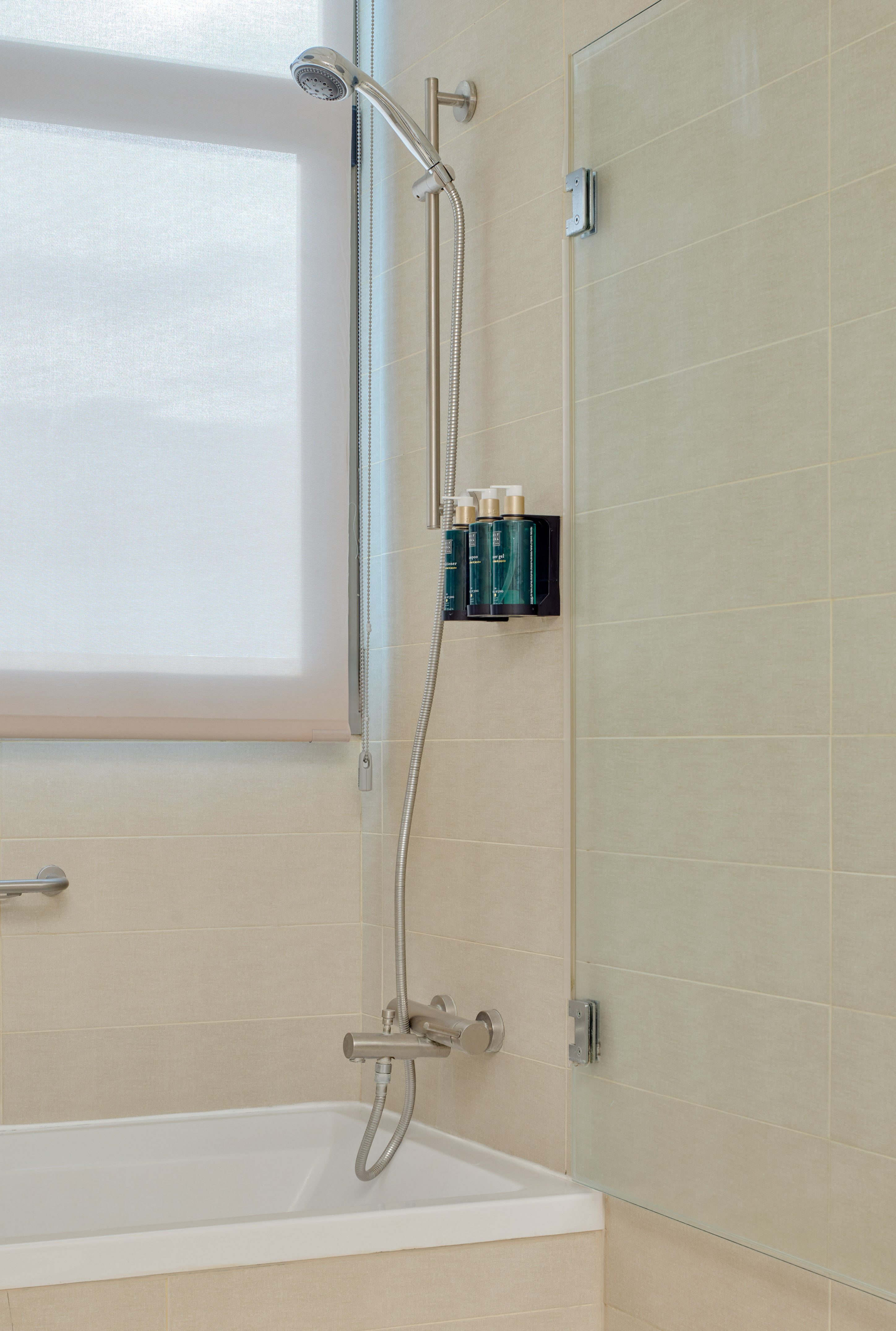 Modern beige tiled bathroom with bathtub, shower, glass screen, and toiletries.