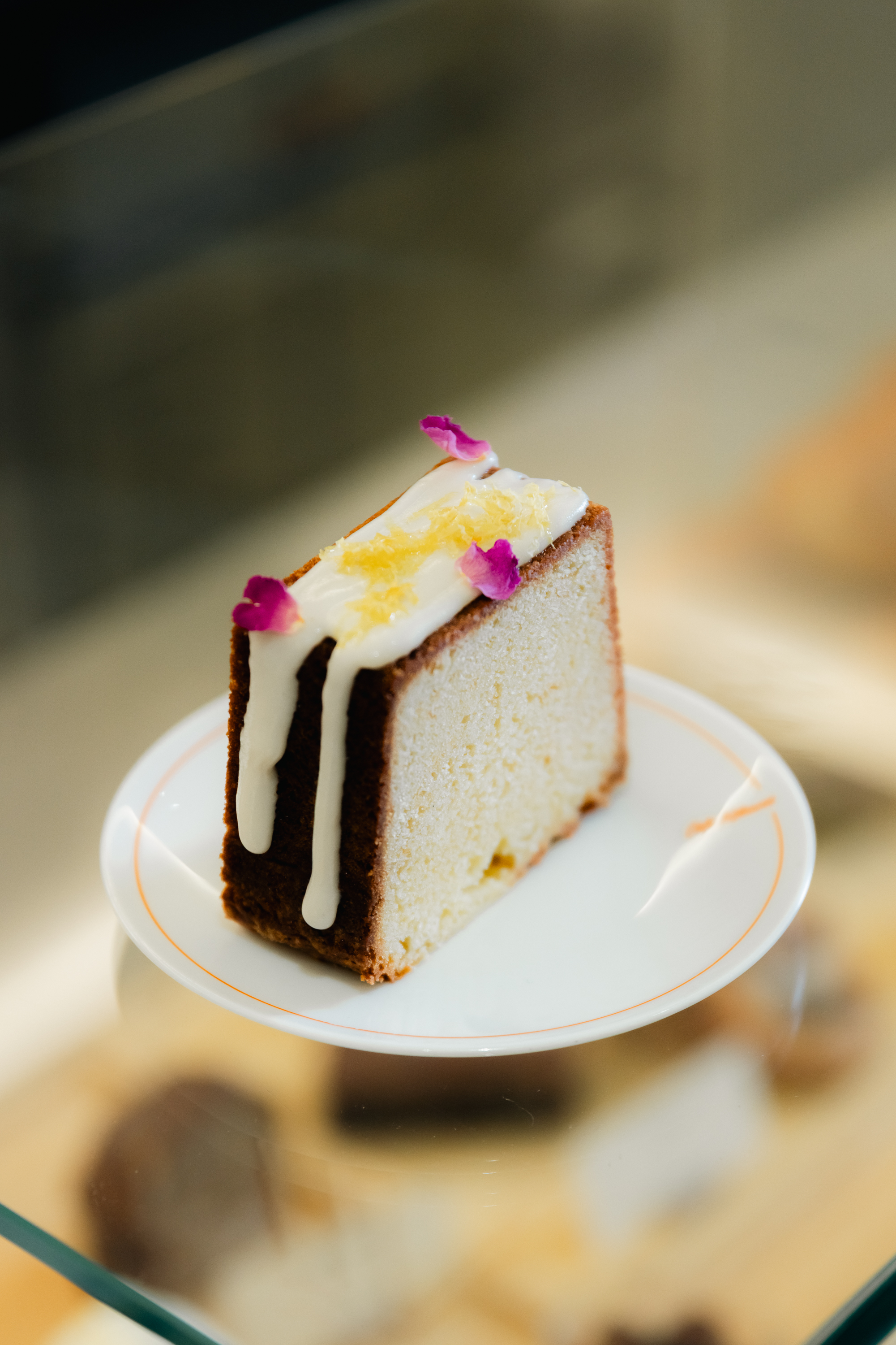 Lemon rose pound cake slice with white glaze, lemon zest, and pink petals.