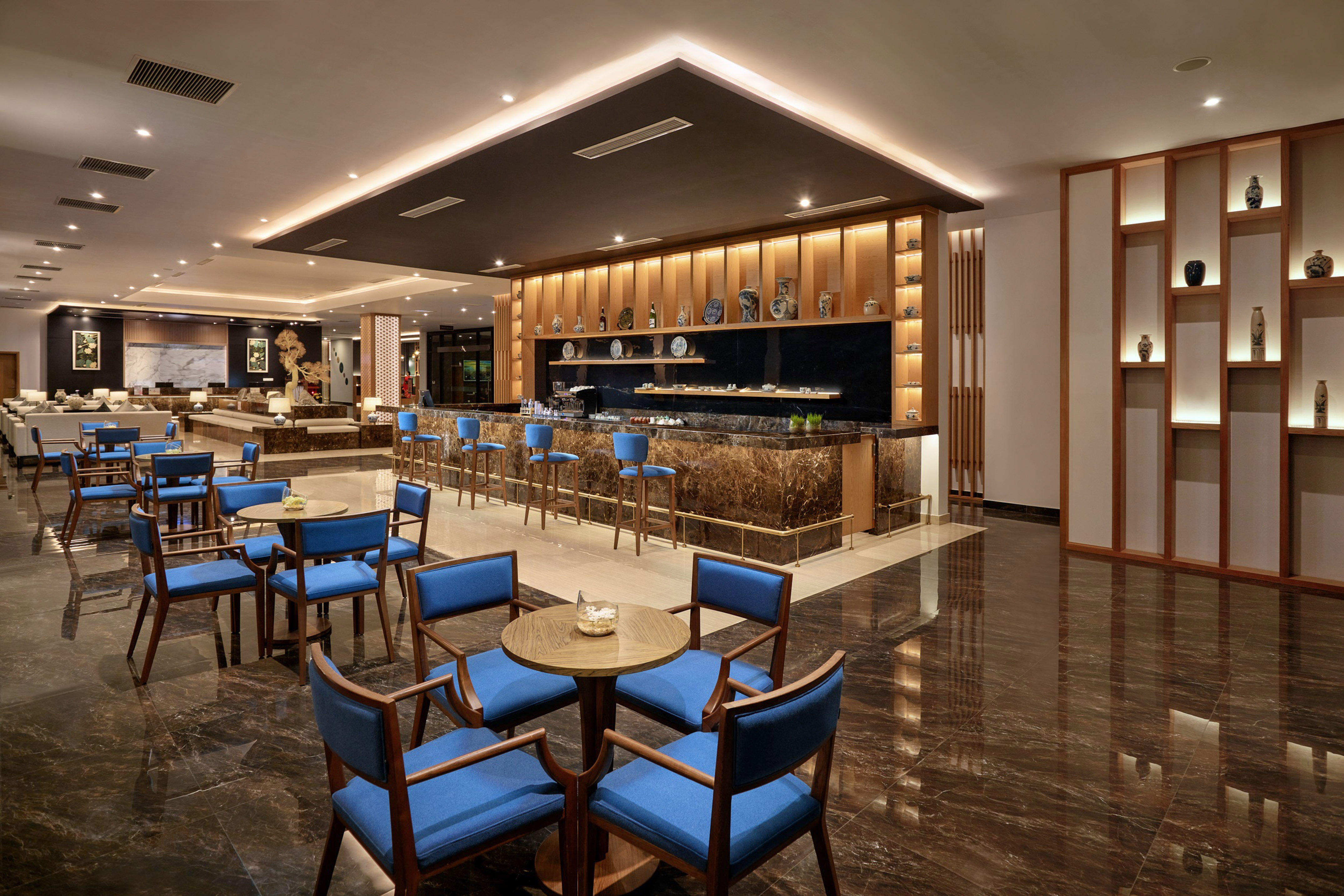 Elegant hotel lobby bar, marble counter, blue chairs, and accent lighting.