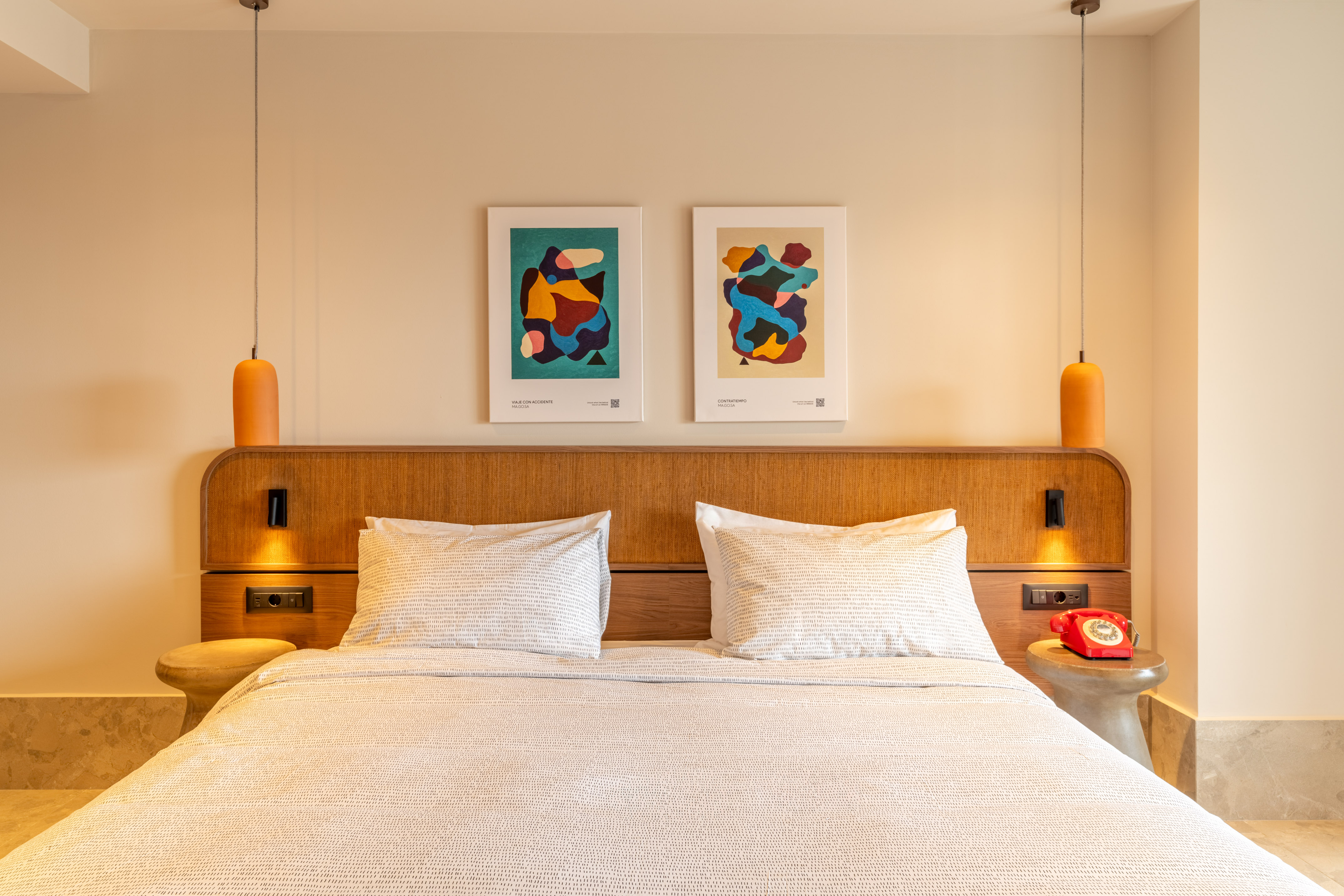 Modern bedroom with white bed, wooden headboard, abstract art, orange lighting.