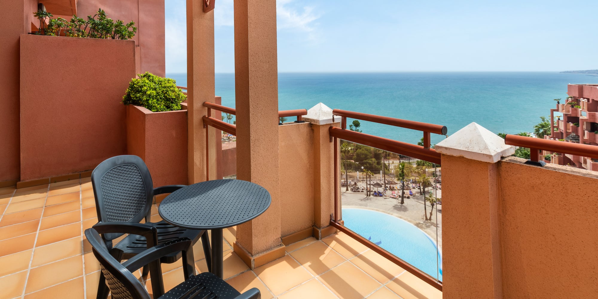 Balcony overlooking ocean and resort pool, with outdoor seating.