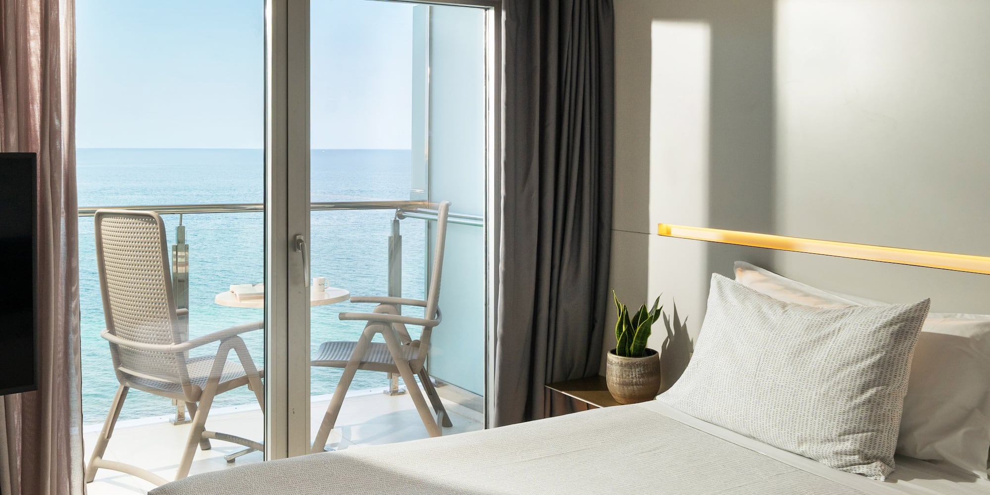 a bed with a glass door and chairs overlooking the ocean