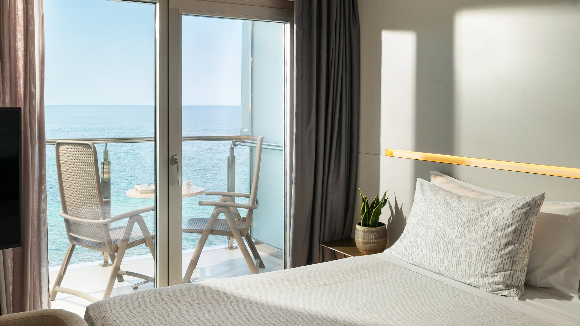 a bed with a glass door and chairs overlooking the ocean