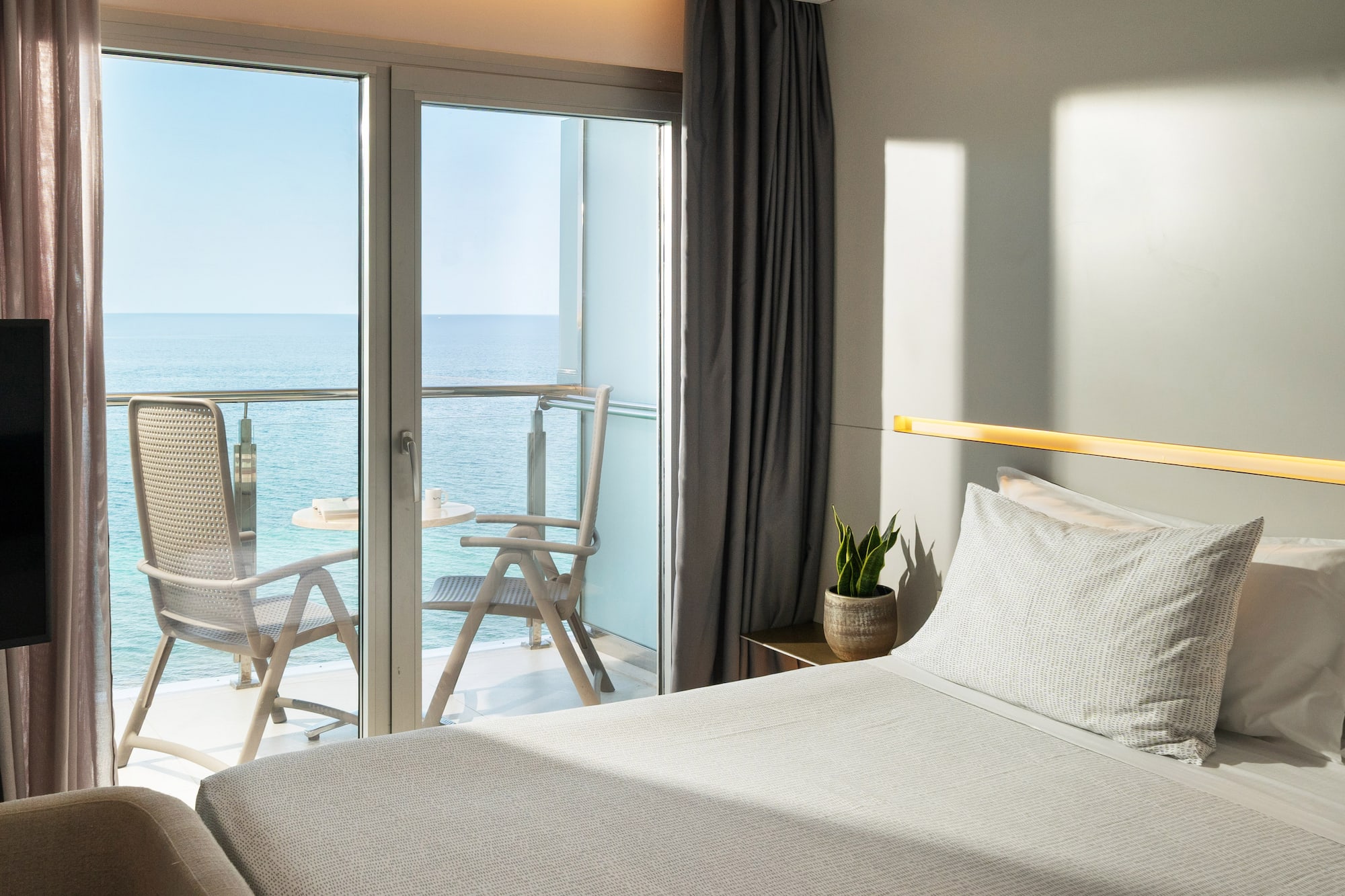 a bed with a glass door and chairs overlooking the ocean