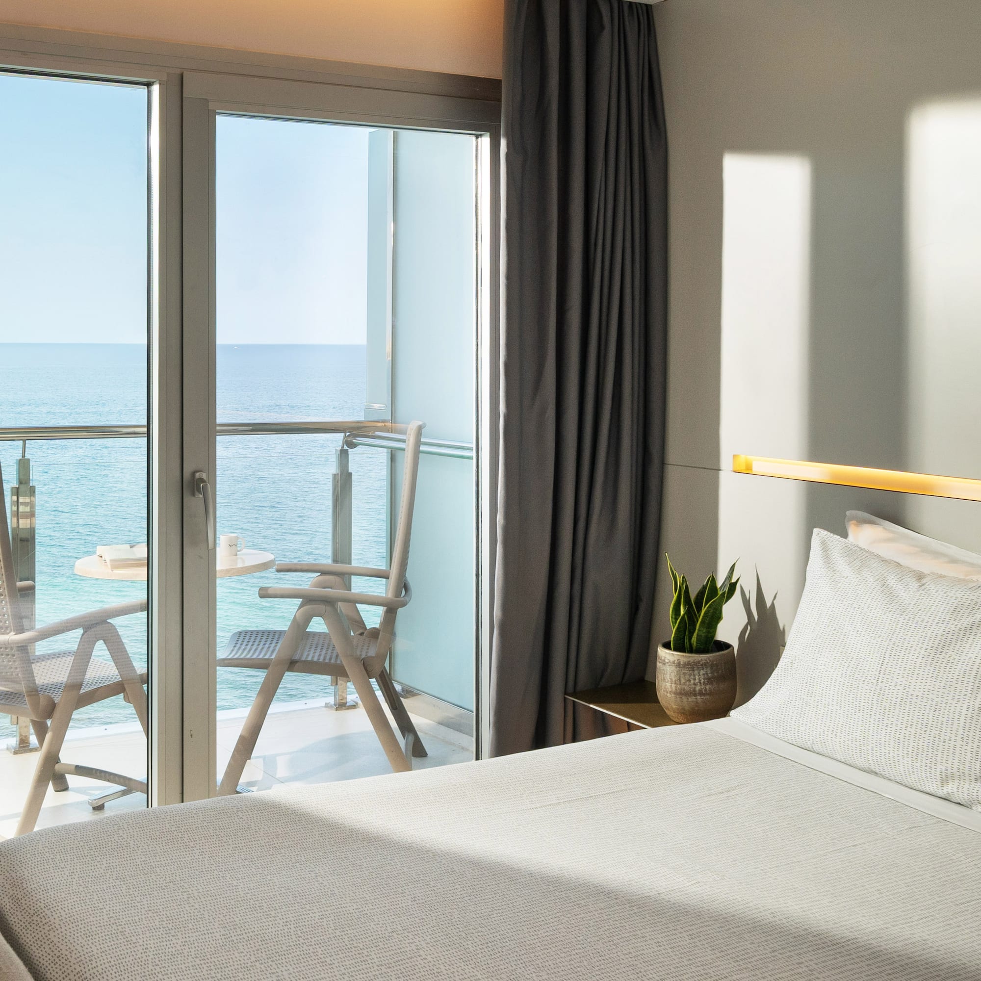 a bed with a glass door and chairs overlooking the ocean