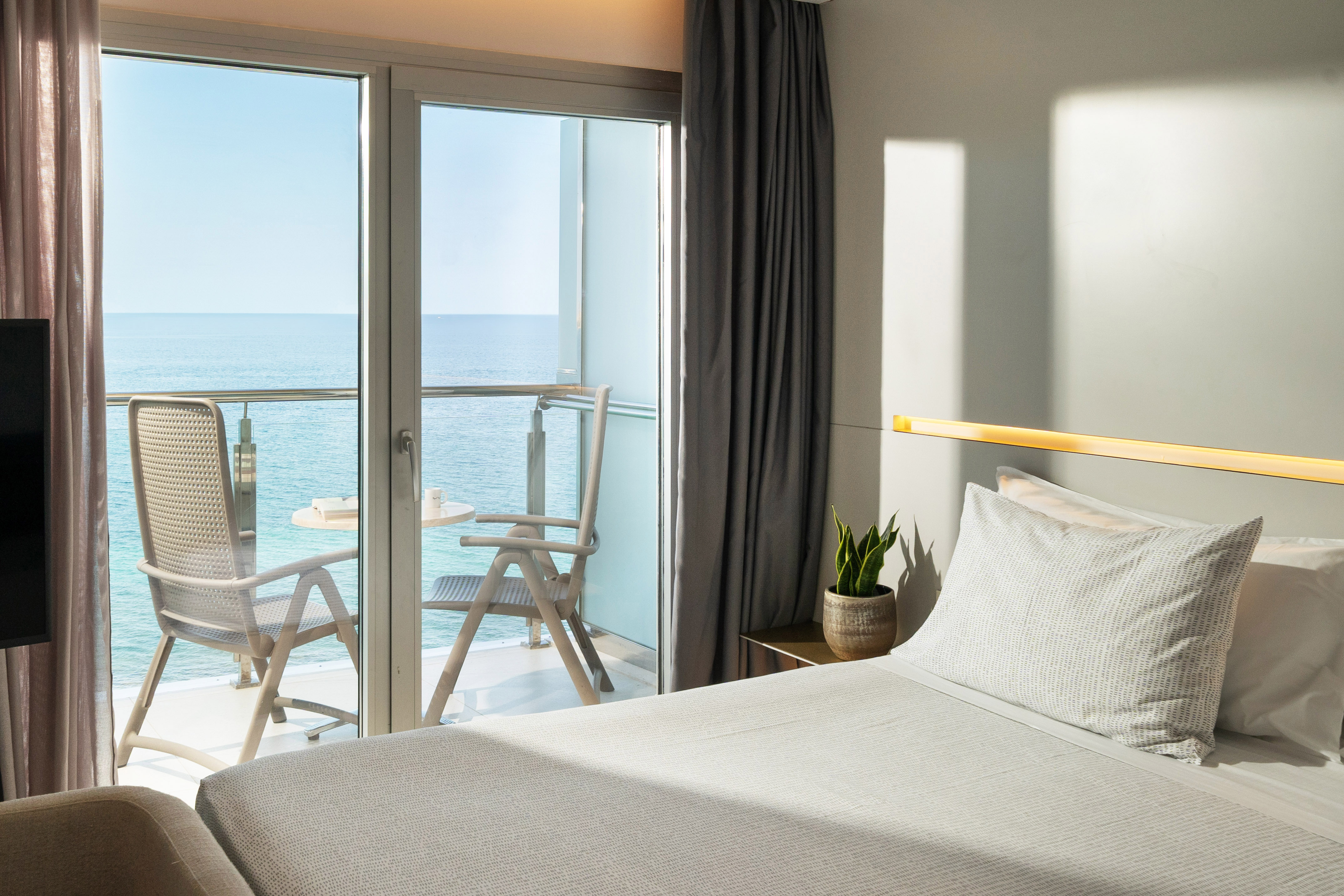 a bed with a glass door and chairs overlooking the ocean