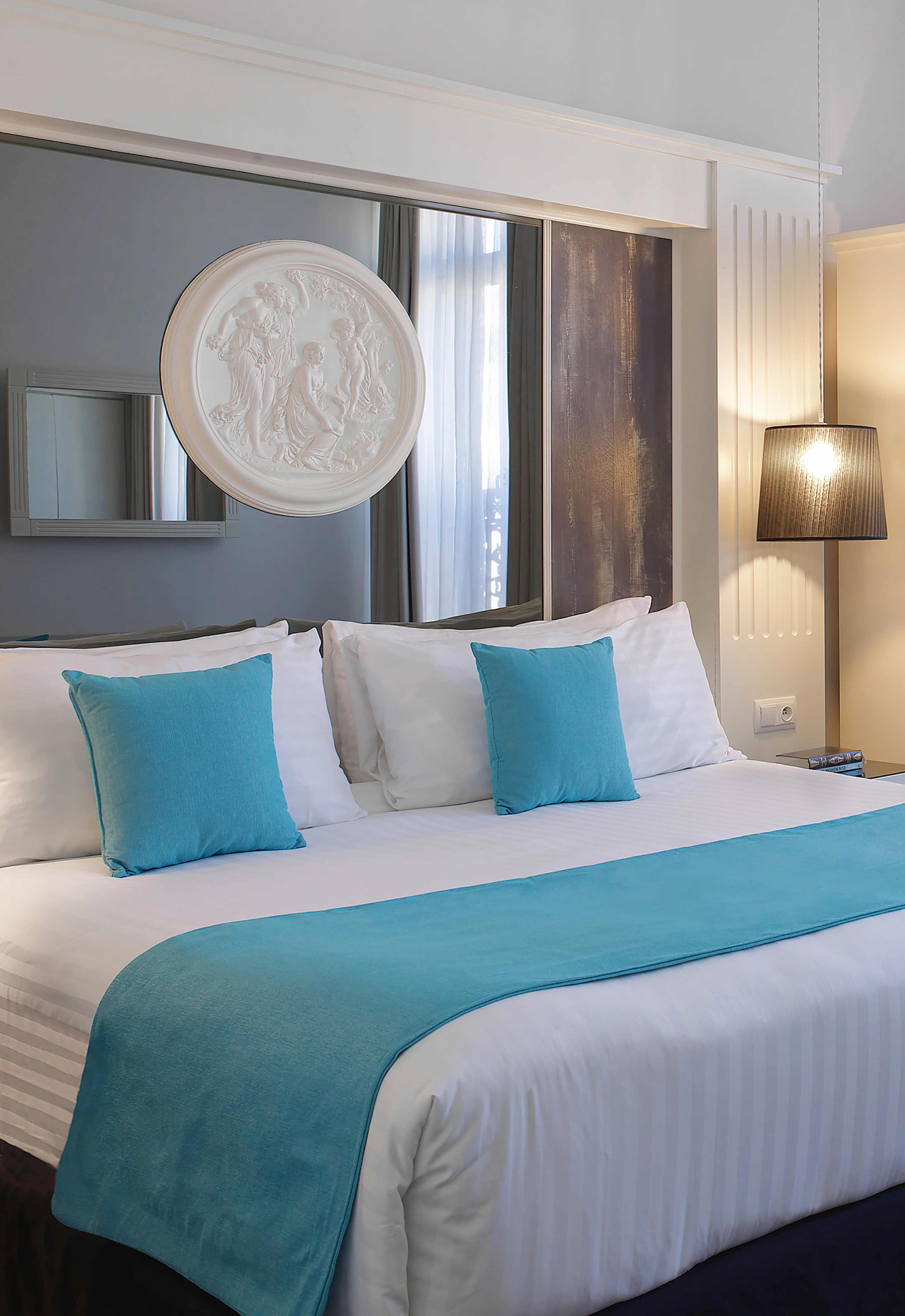 Luxurious hotel bedroom with white bedding, turquoise accents, and classical art.