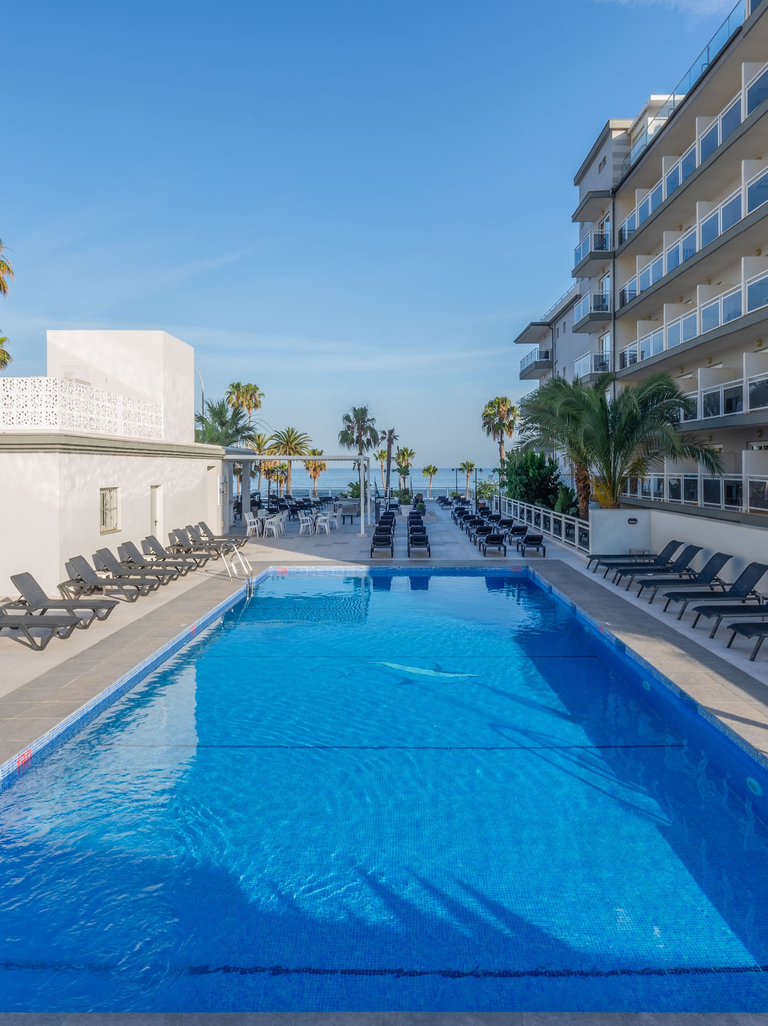 a swimming pool with chairs and a building with palm trees